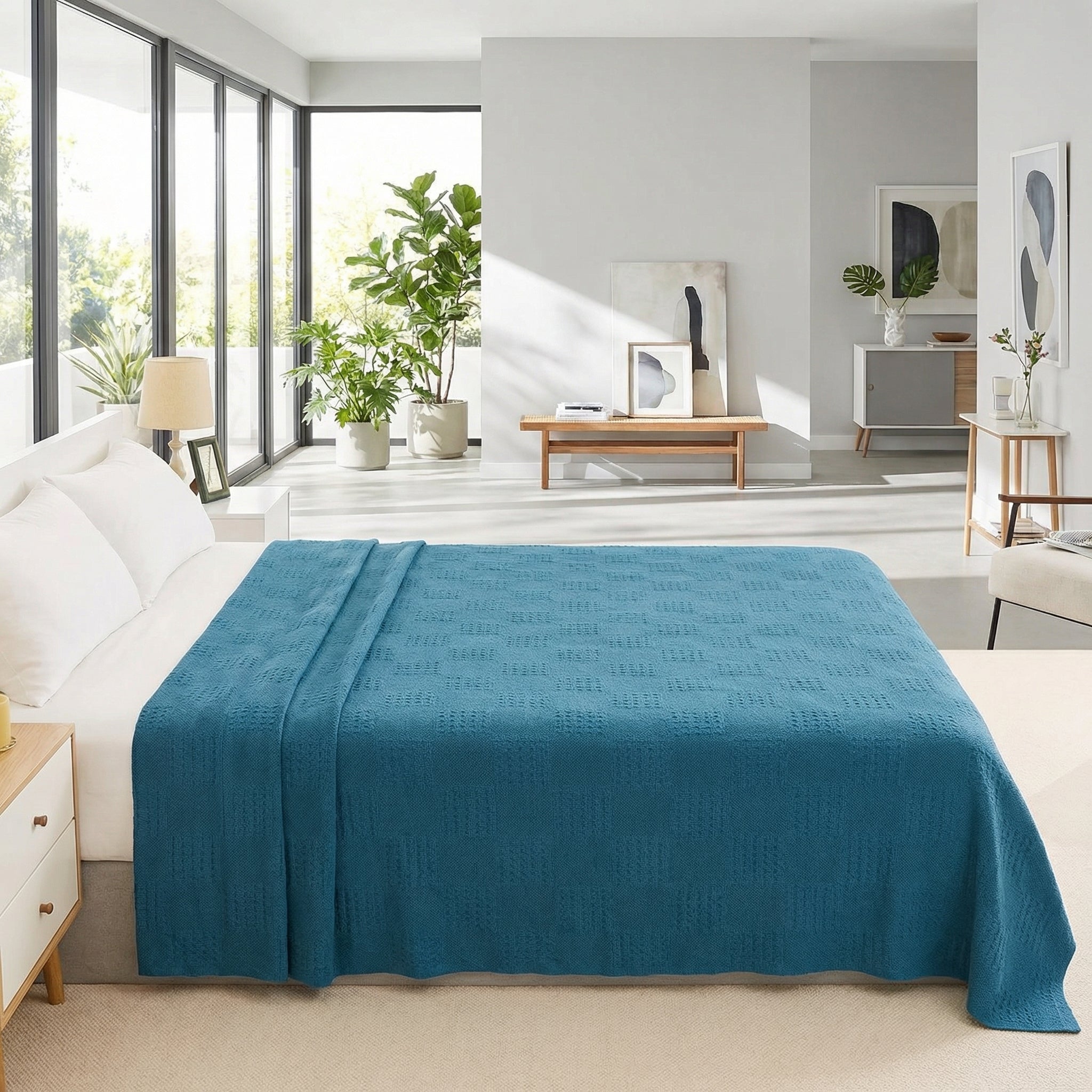 Teal hollow knit cotton summer blanket draped over a bed in a bright, modern bedroom.