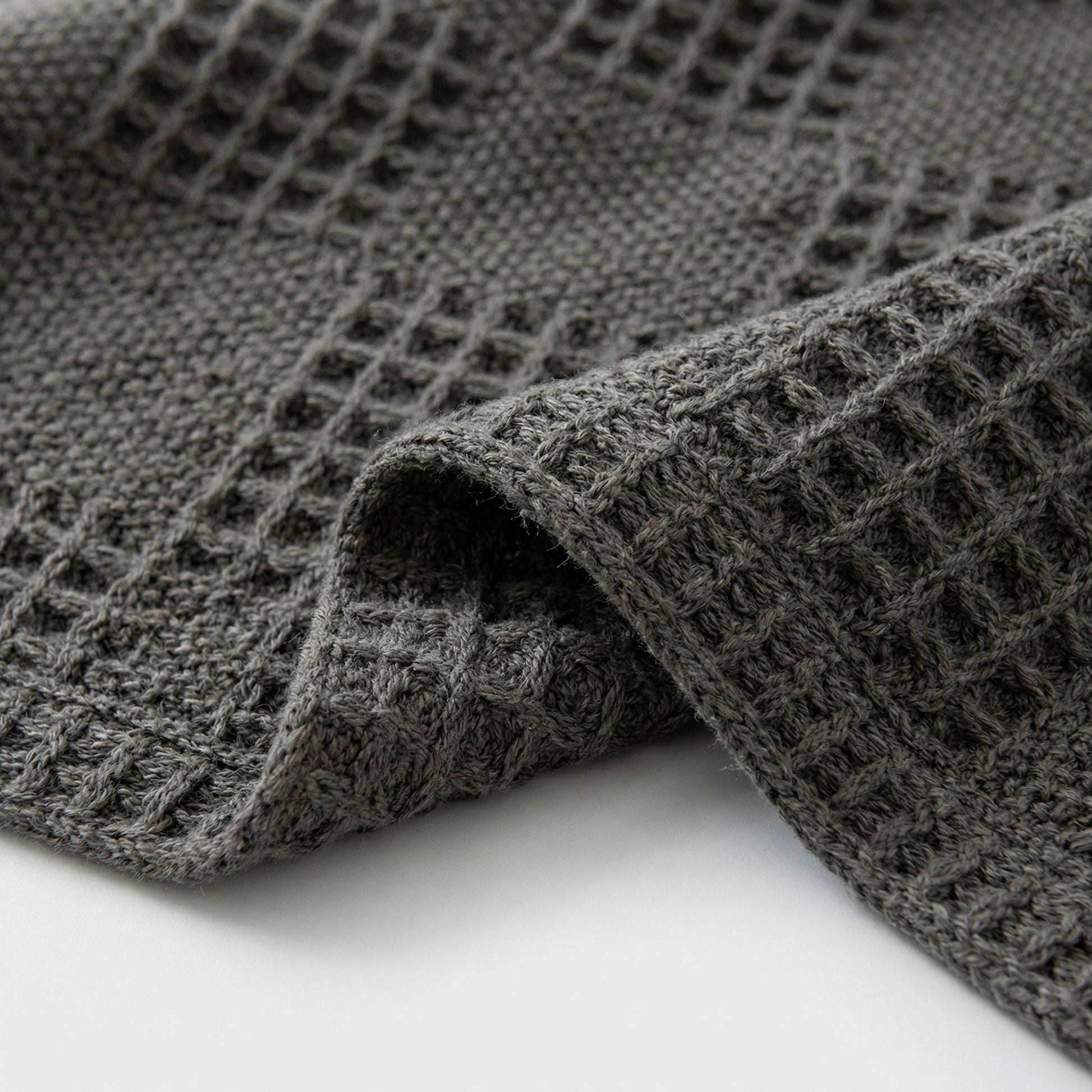 Close-up of a folded dark gray cotton hollow knit summer blanket with a textured waffle pattern.