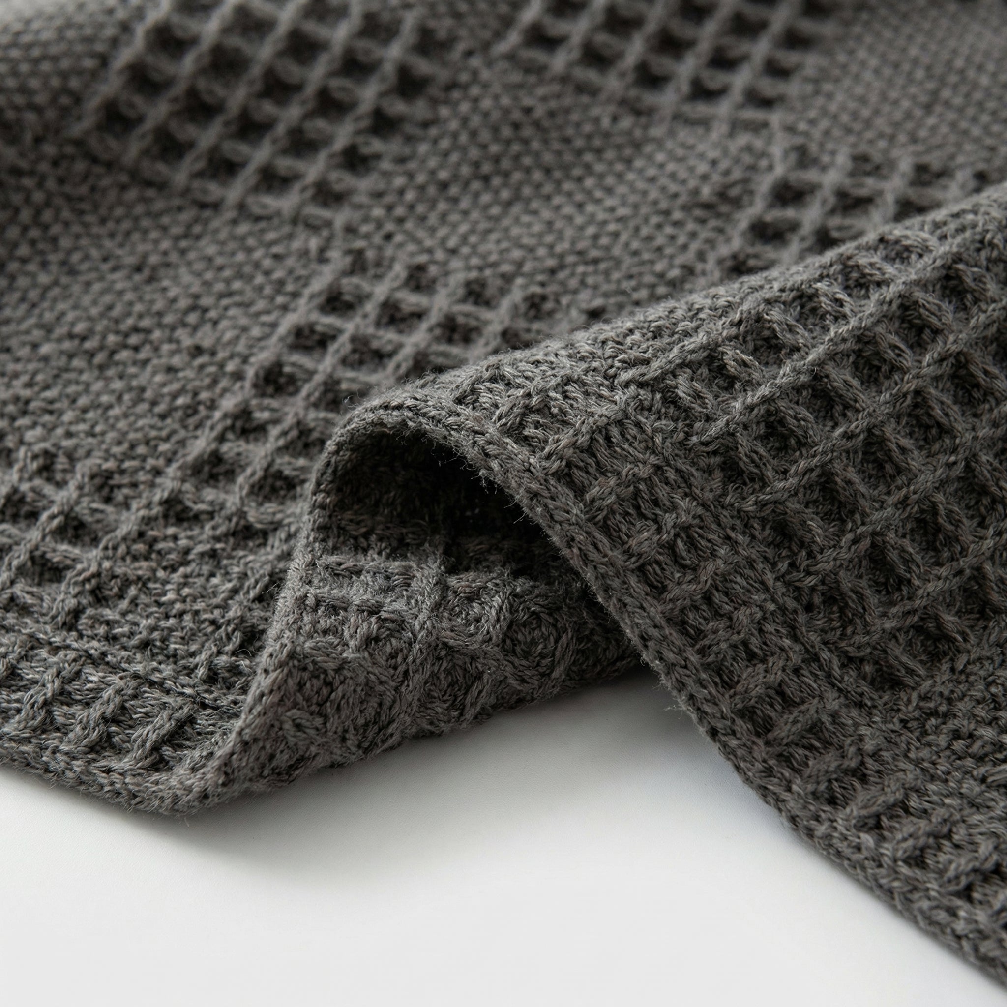 Close-up of a folded dark gray cotton hollow knit summer blanket with a textured waffle pattern.