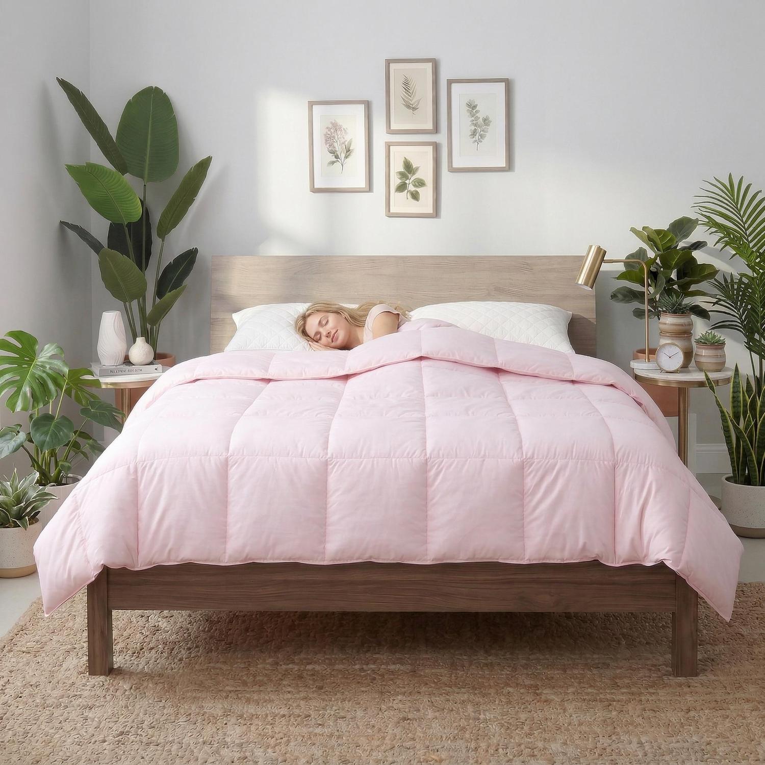 Woman sleeping peacefully under a soft, plush pink box-stitched down comforter on a wooden bed.