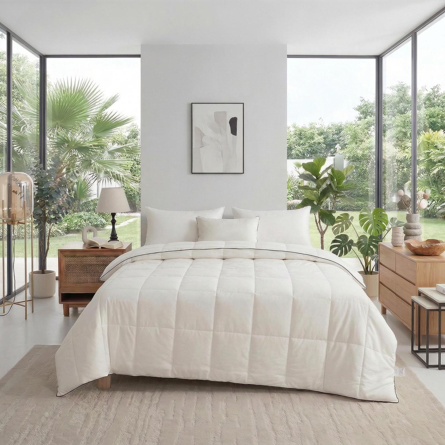 White quilted cooling quilt on a bed in a bright, modern bedroom with large windows and plants.