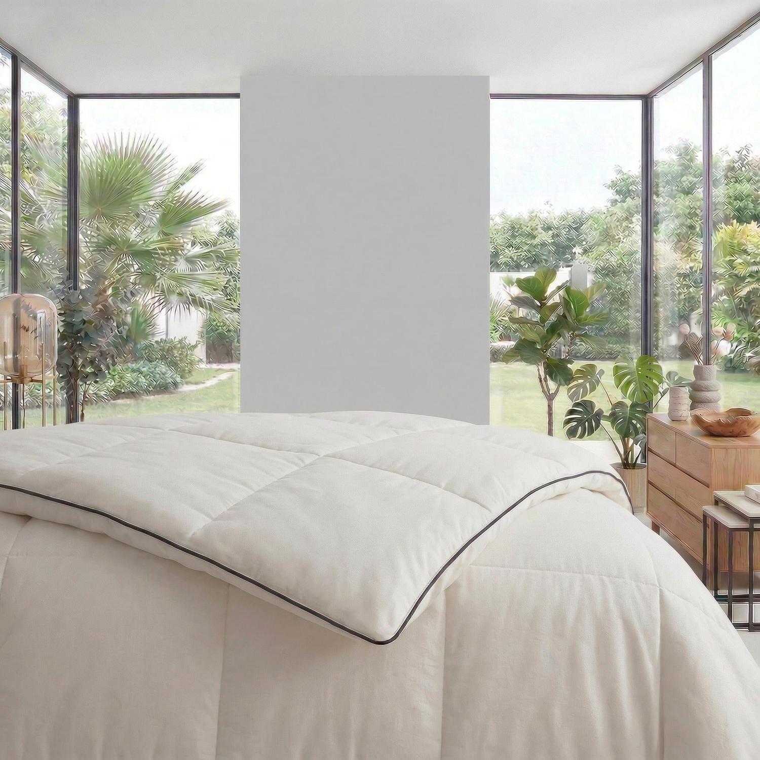 White quilted cooling blanket with black trim on a bed in a bright bedroom with large windows.