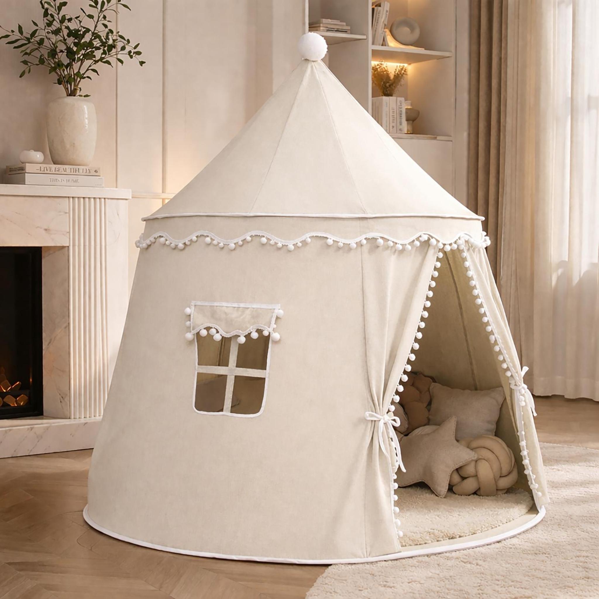 Cream fabric kids indoor play tent with pom-pom trim, a small window, and an open entrance with ties.