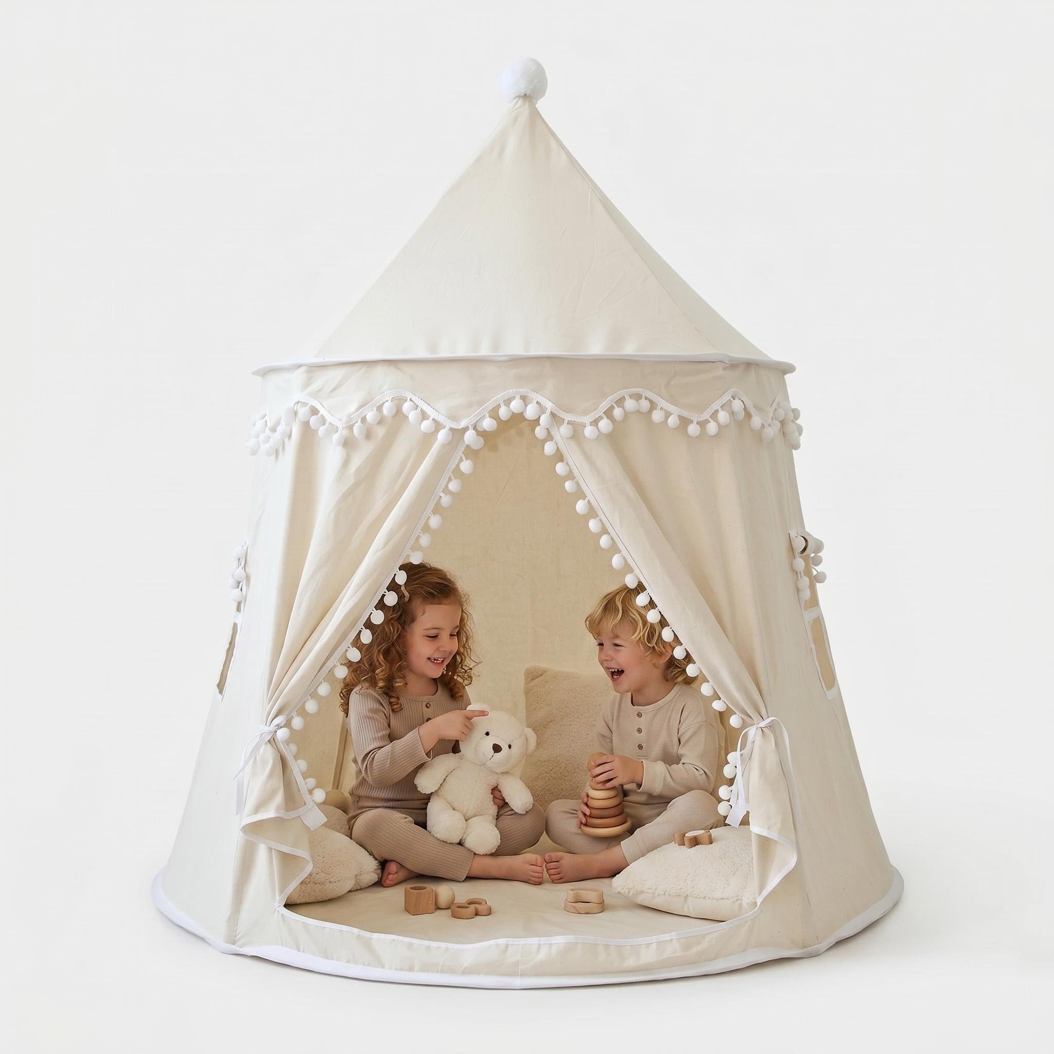 Cream indoor play tent with pom-pom trim, two children playing inside with a teddy bear and wooden toys.