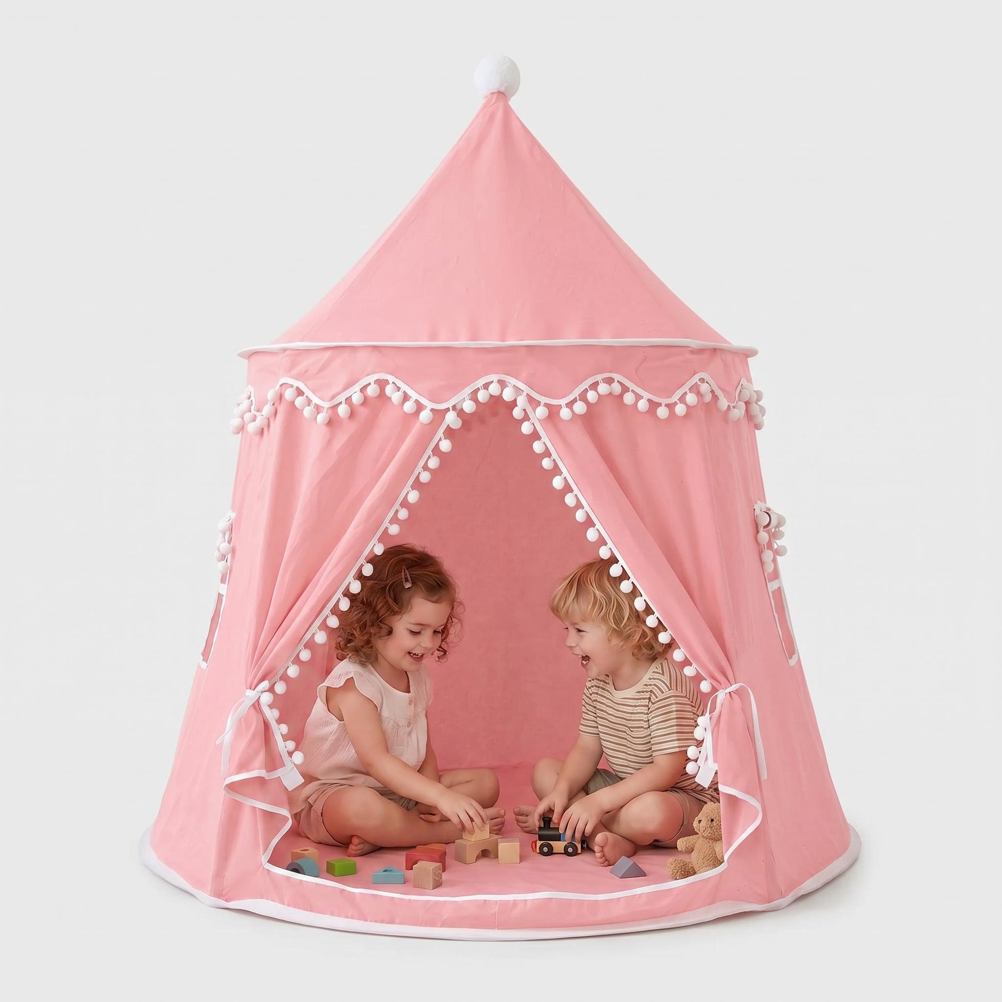 Pink indoor play tent with white pom-poms, a child playing inside with blocks.