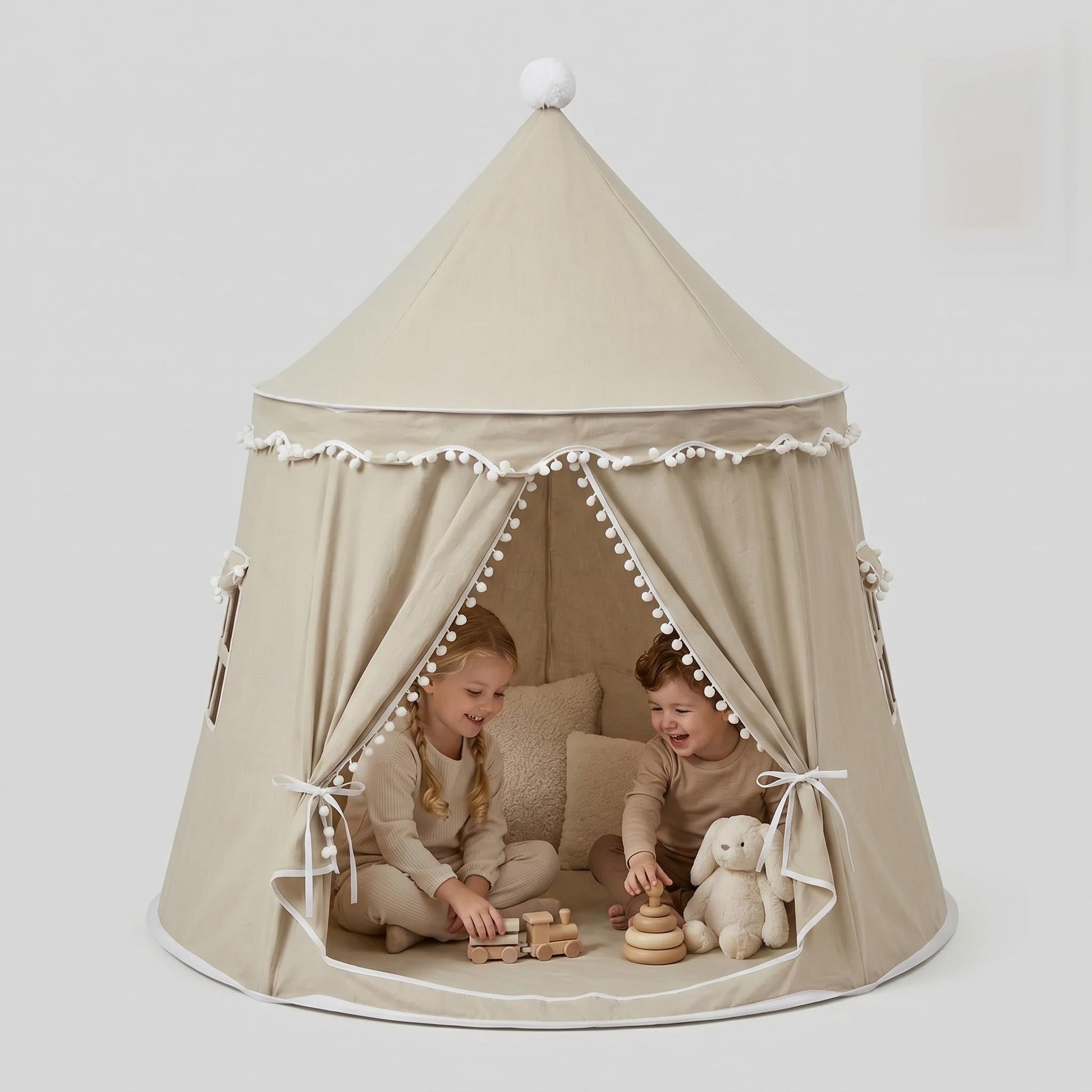 Two children playing inside a beige indoor play tent with white trim, pom-poms, and a top pom-pom.