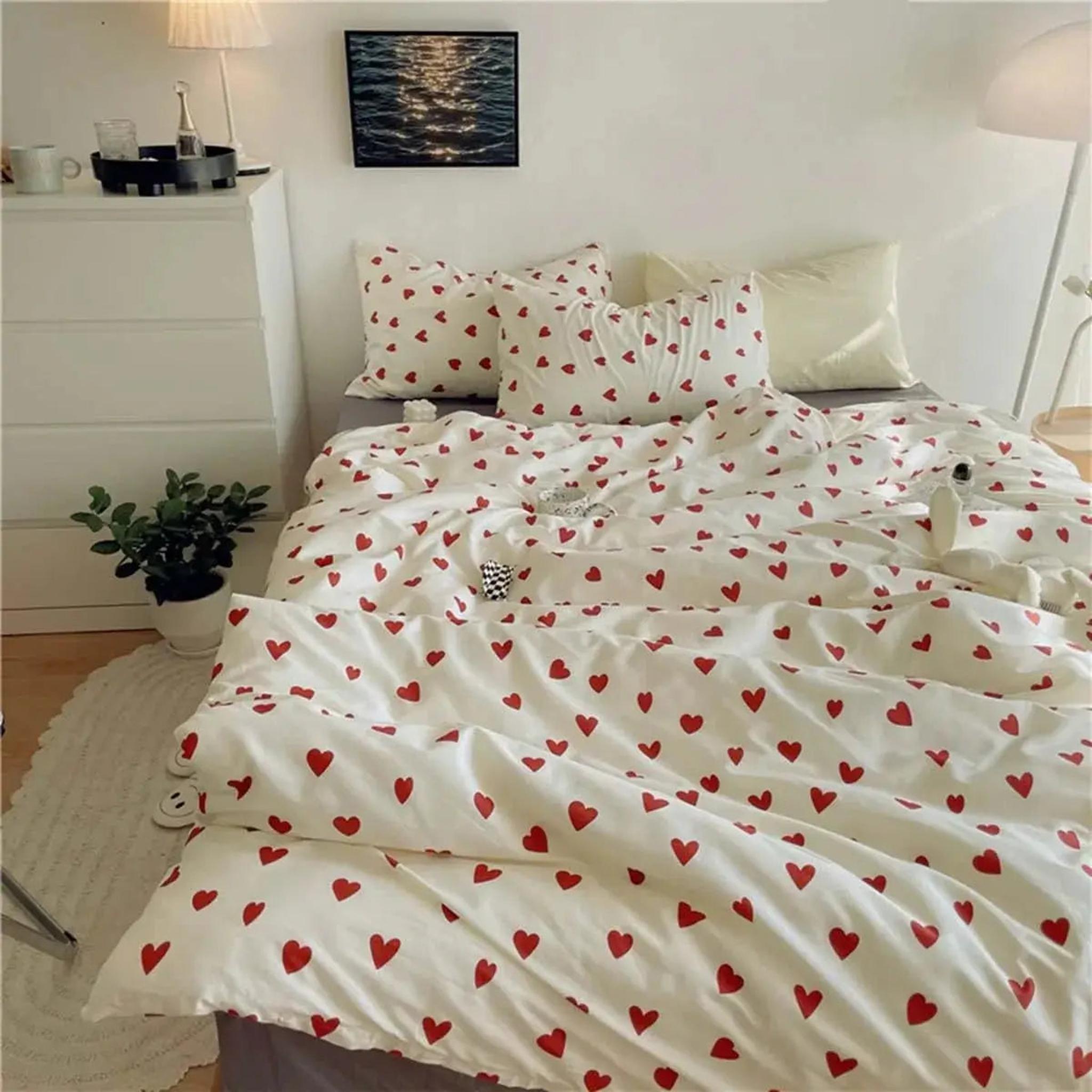 White microfiber bedding set with red heart pattern, including duvet cover and pillowcases, on a bed.
