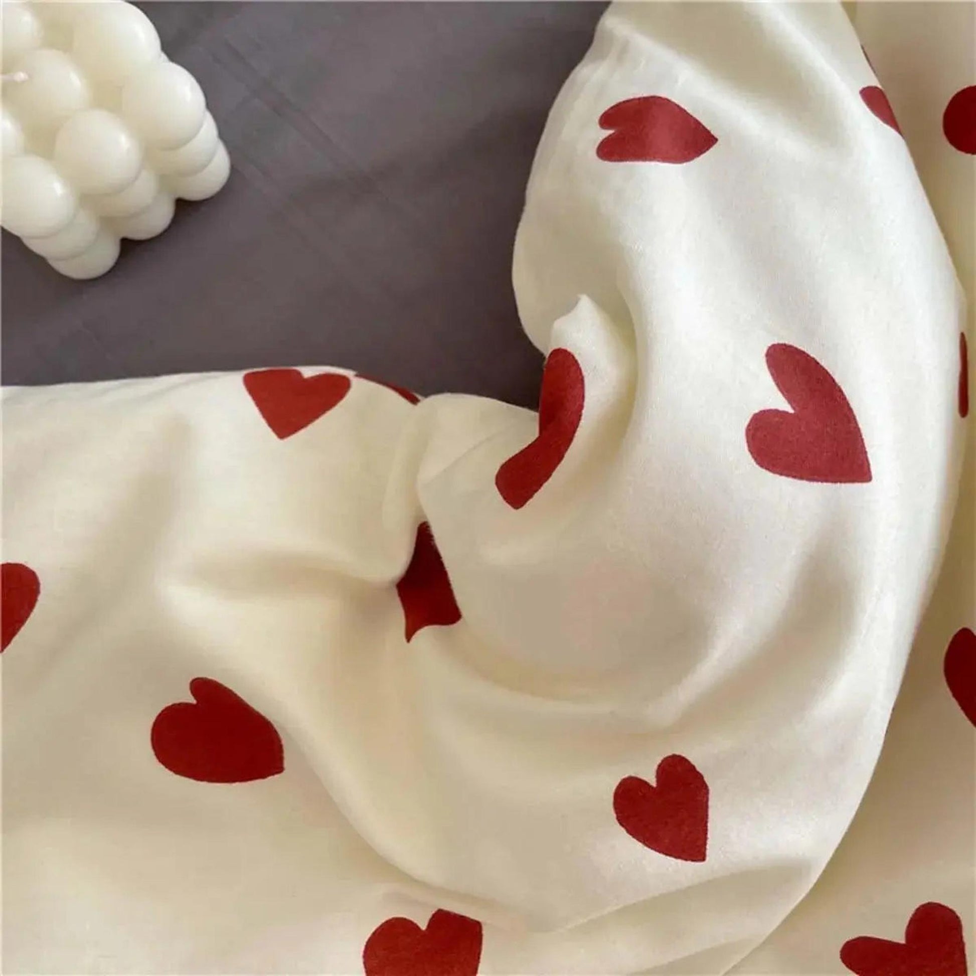 Cream microfiber bedding with red heart pattern, draped over a gray sheet, next to a white bubble candle.