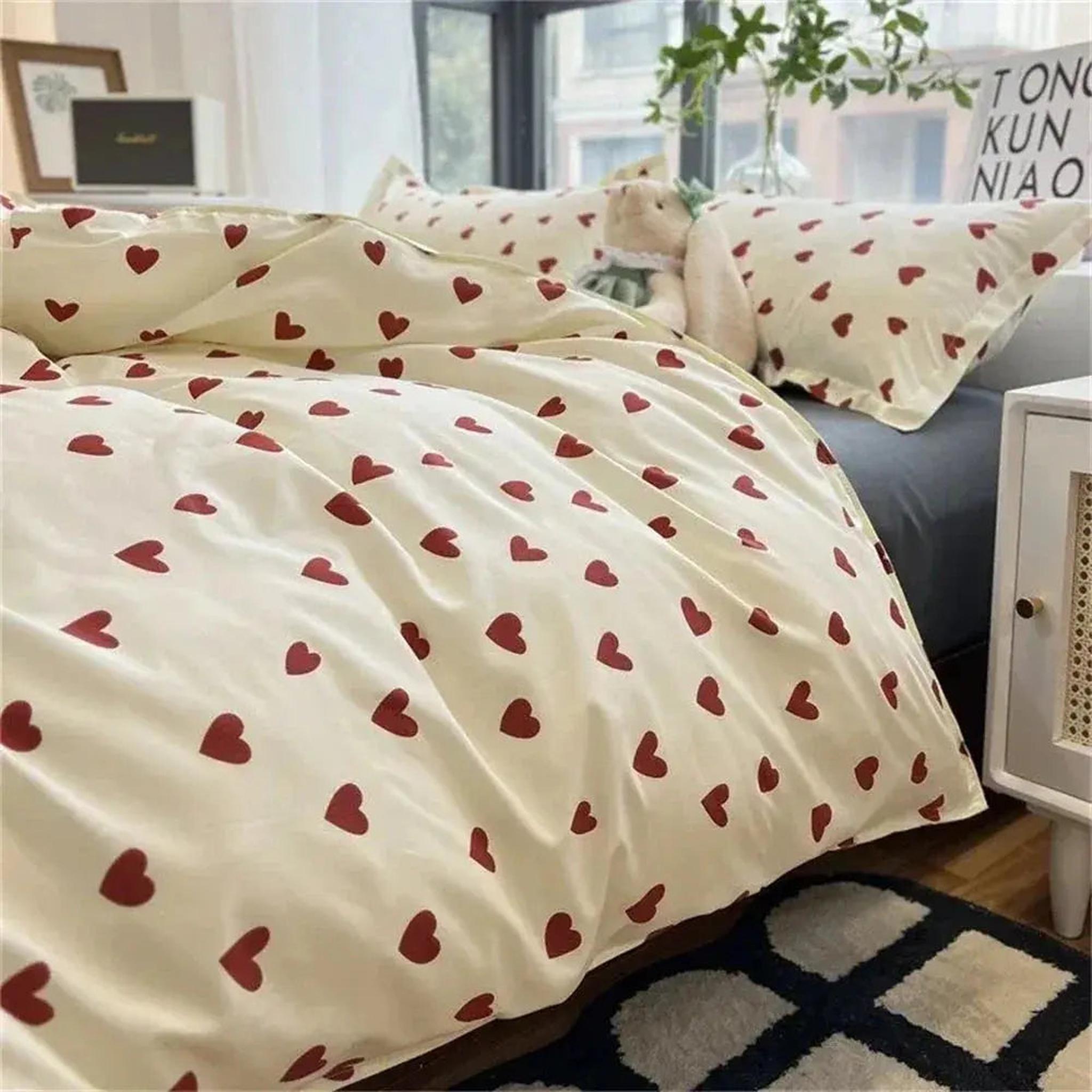 Cream microfiber bedding set with red heart pattern, including duvet cover and pillowcases, on a bed.