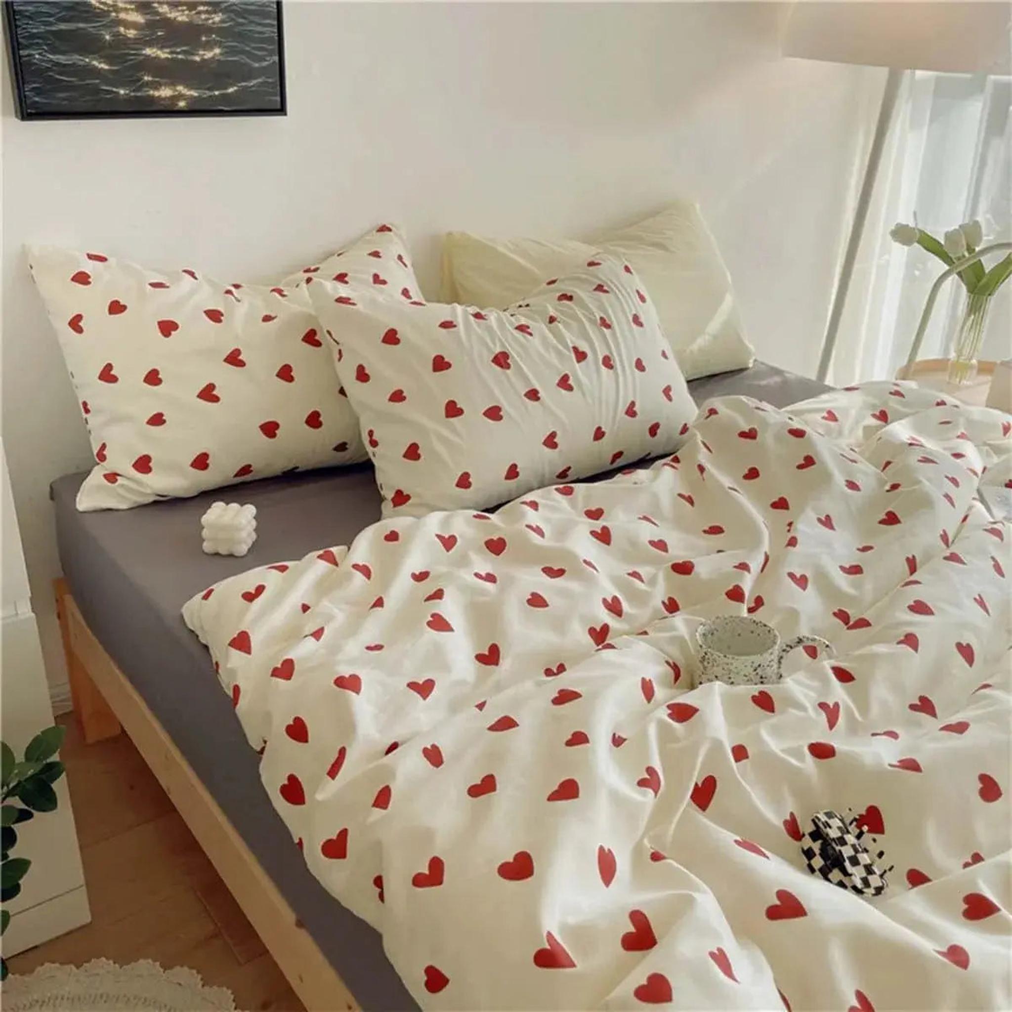 White microfiber bedding set with red heart pattern, including duvet cover and two pillowcases, on a wooden bed frame.