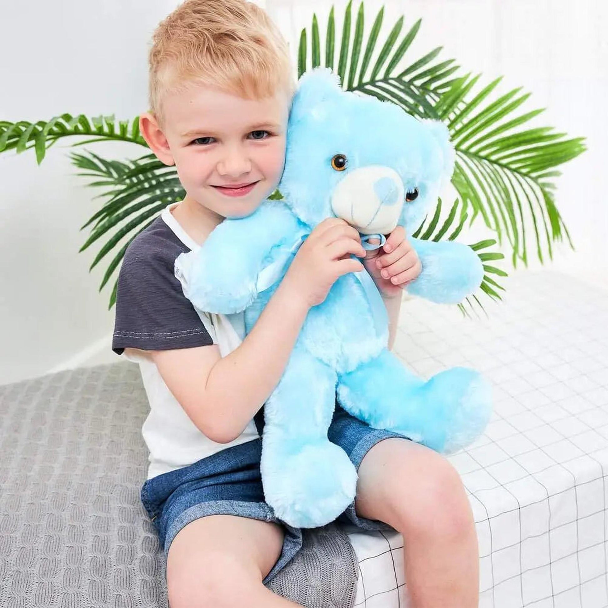 Smiling boy hugging a soft, light blue LED glowing plush teddy bear with brown eyes.