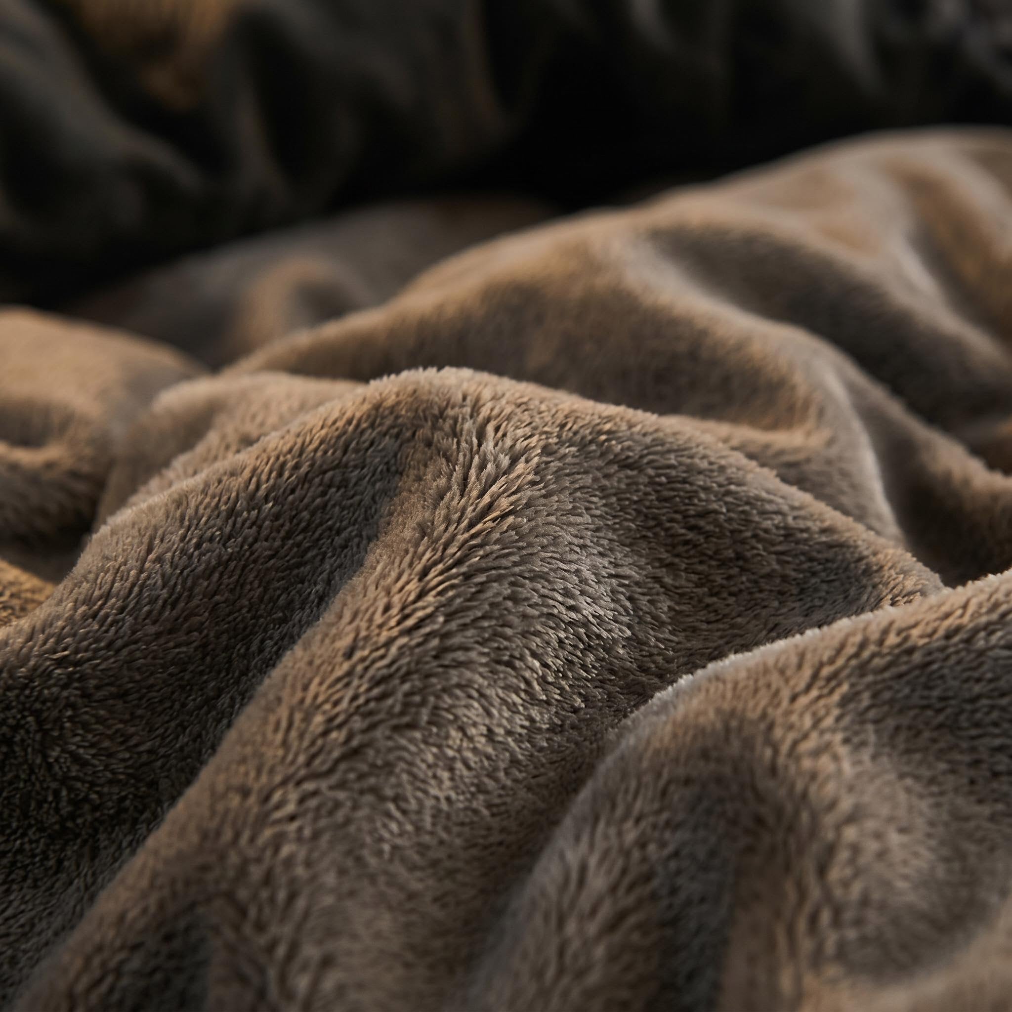 Close-up of a soft, textured brown lamb wool fleece blanket in folds.