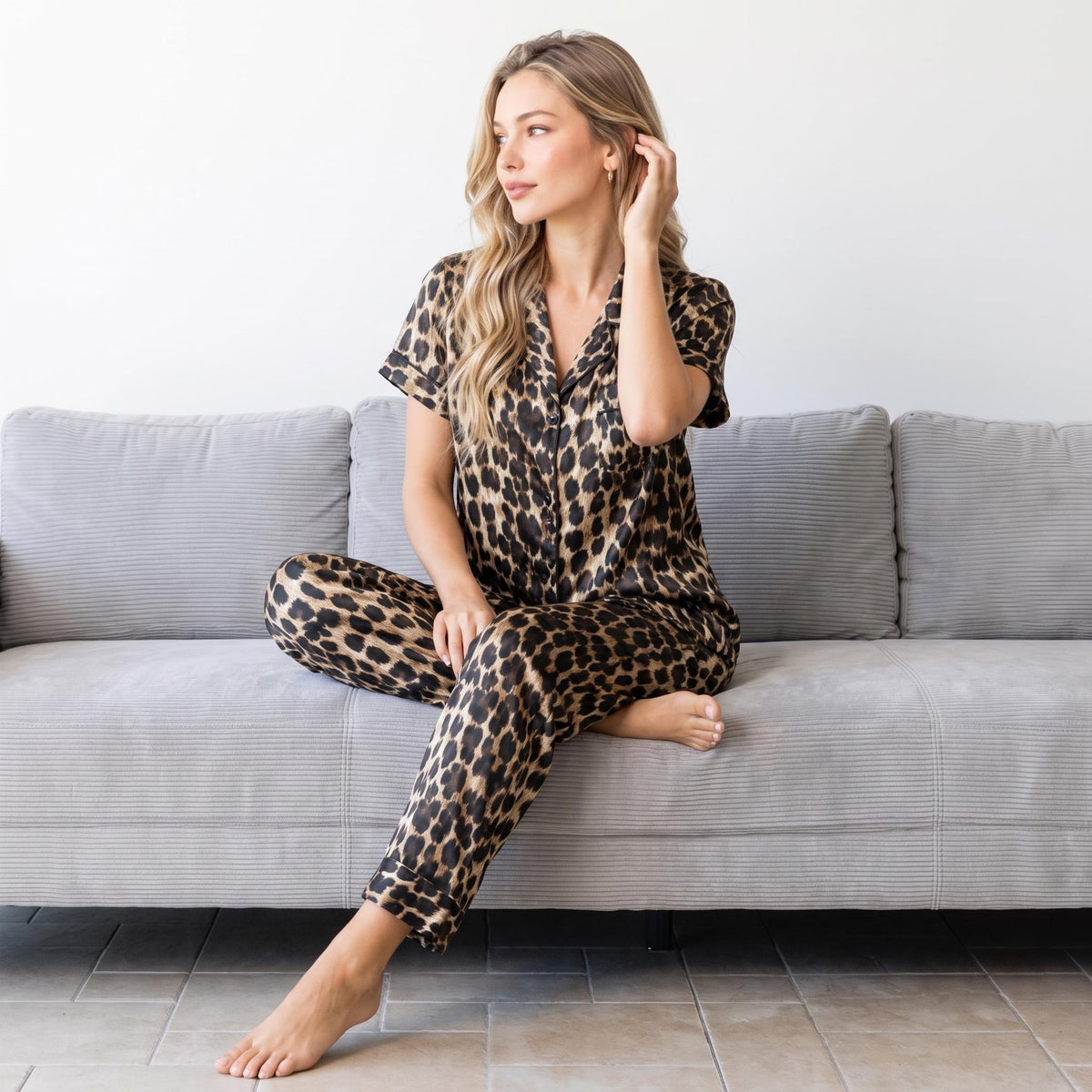Woman wearing a leopard print Mulberry silk pajama set with a short-sleeve button-down shirt and matching pants on a sofa.