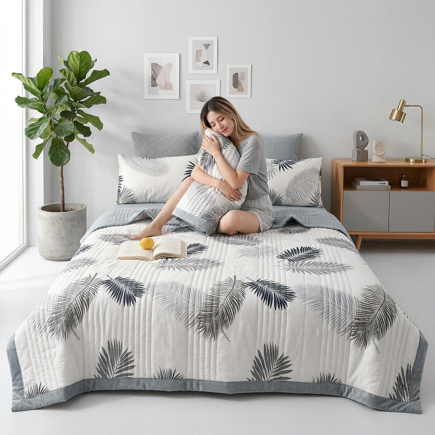 White lightweight summer quilt with grey palm leaf pattern, grey trim, and matching pillow shams on a bed.