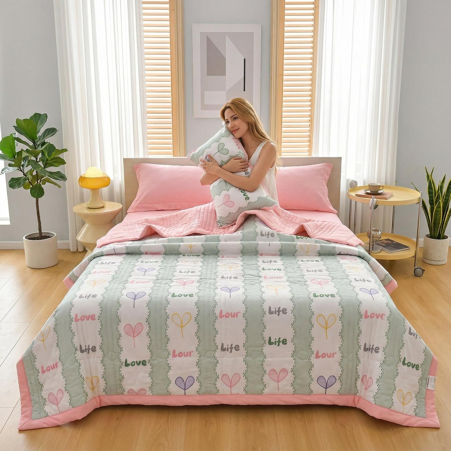 Woman on a bed with a pink and green patchwork summer quilt featuring "Love Life" text and heart designs.