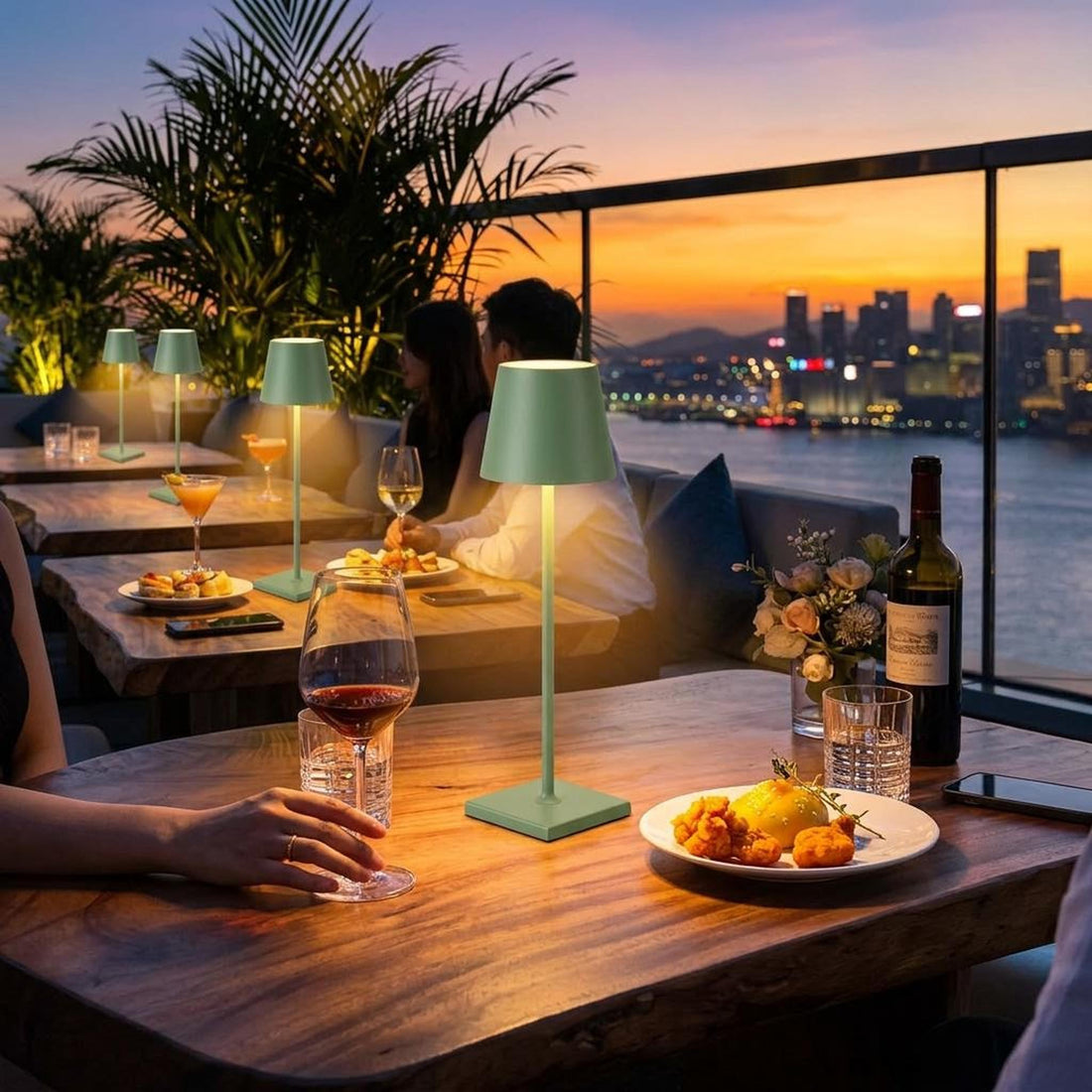 Sage green portable LED table lamp with a minimalist aluminum design on an outdoor dining table at sunset.
