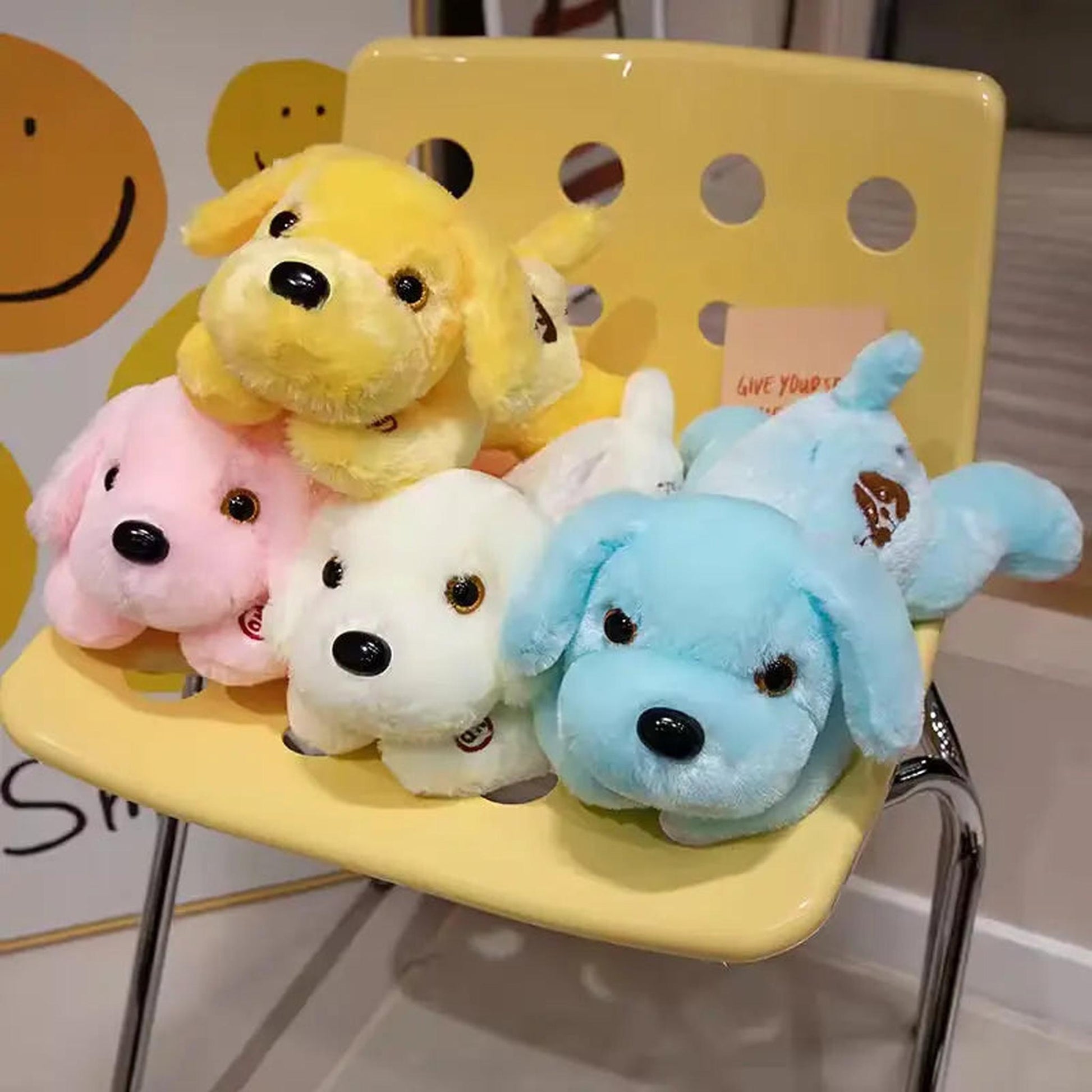 Five colorful, soft plush dog pillows in yellow, pink, white, and blue resting on a yellow chair.