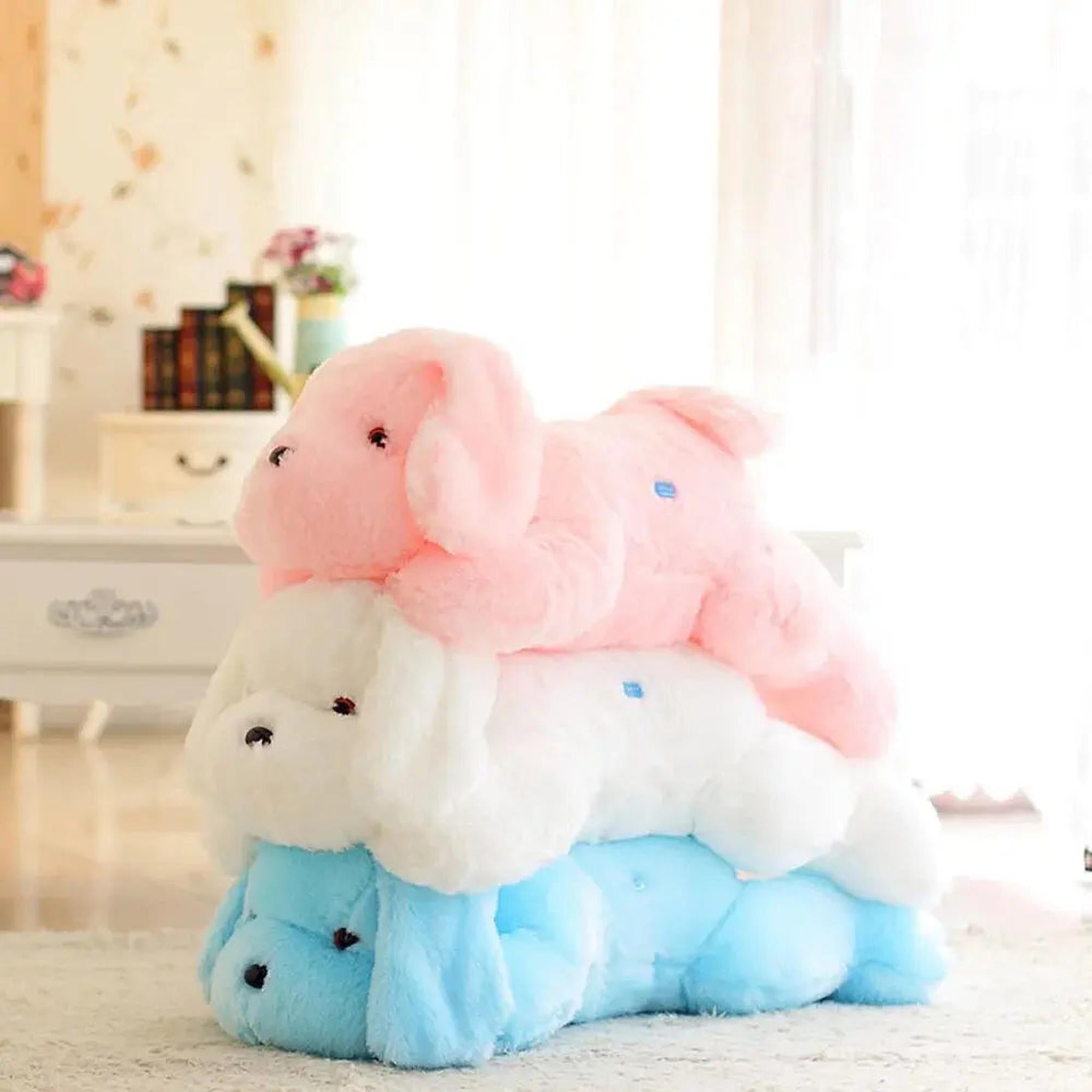 Stack of three soft, plush dog pillows in pink, white, and blue colors on a light-colored floor.
