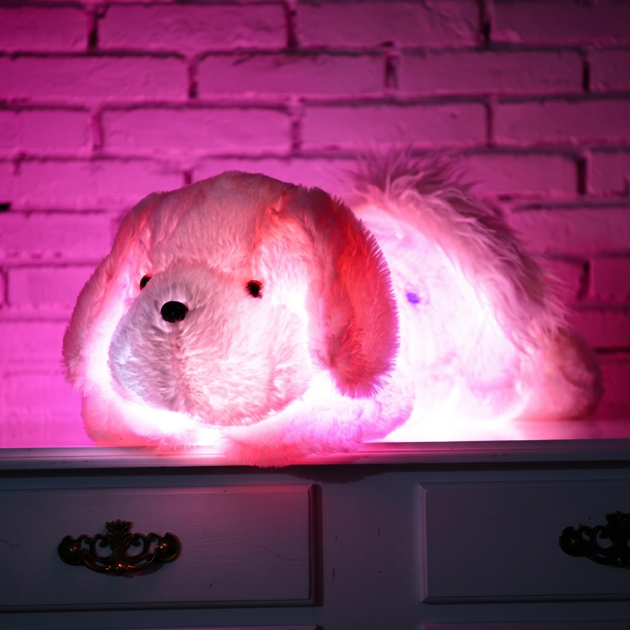 Glowing white plush dog pillow with pink LED light on a dresser against a brick wall.