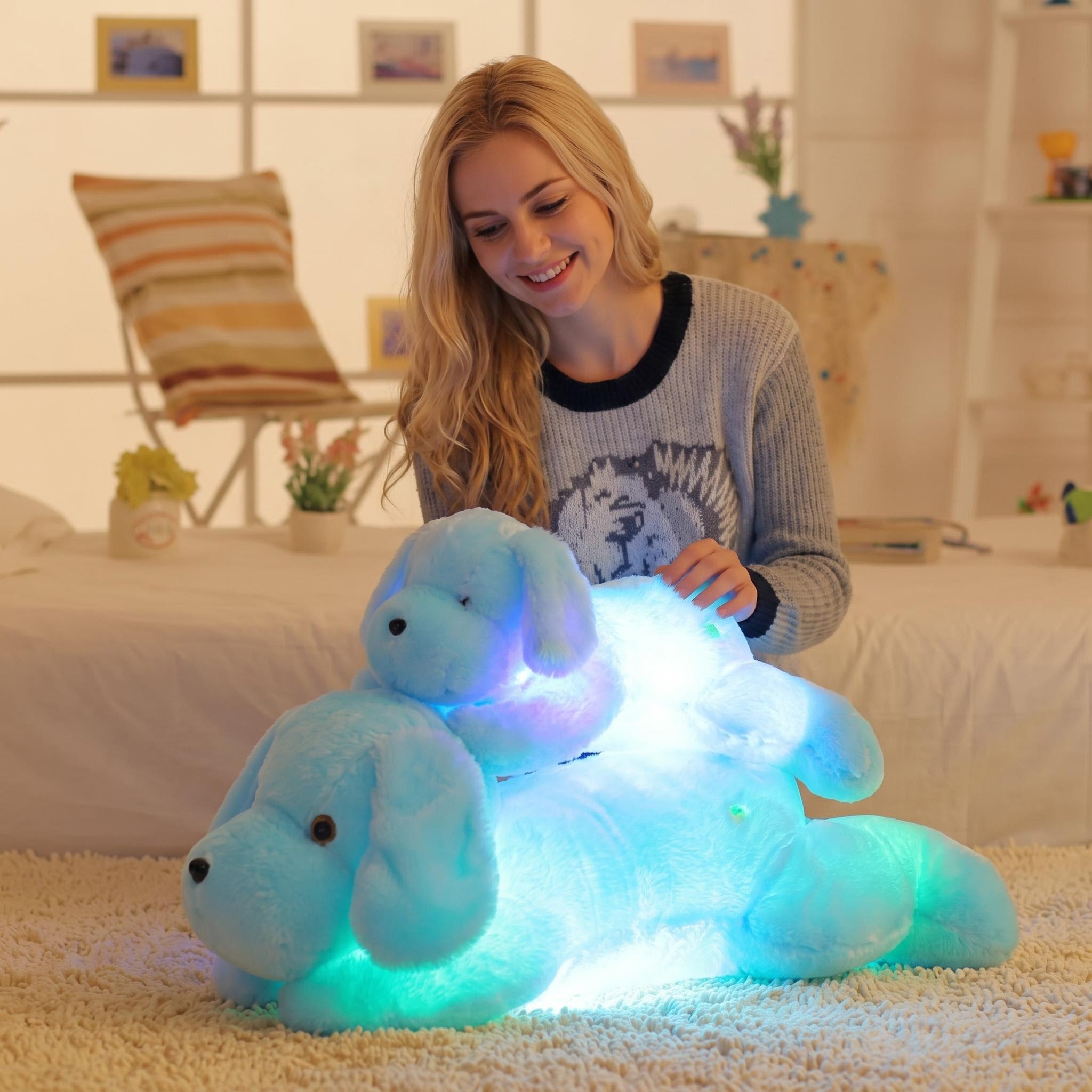 Smiling woman with glowing blue luminous dog plush pillows in a cozy room.