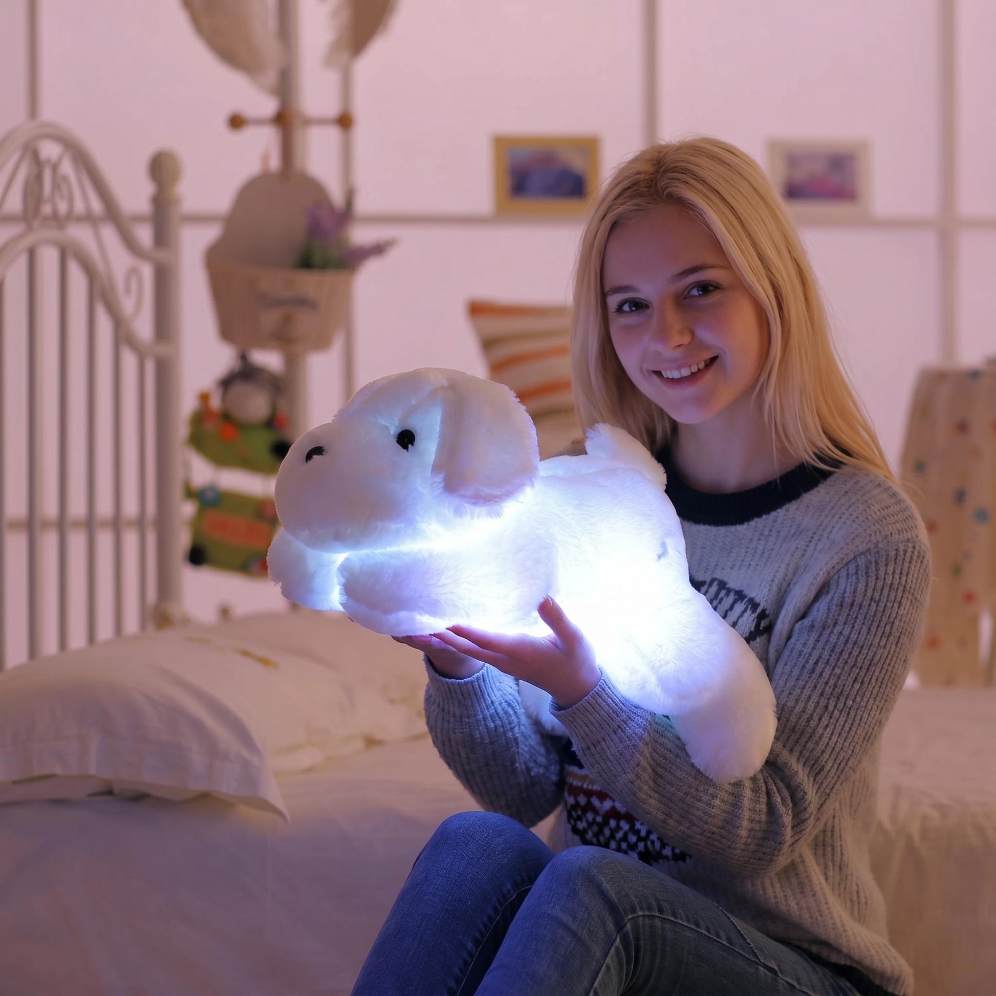 Smiling girl holding a glowing white luminous dog plush pillow in a cozy bedroom.