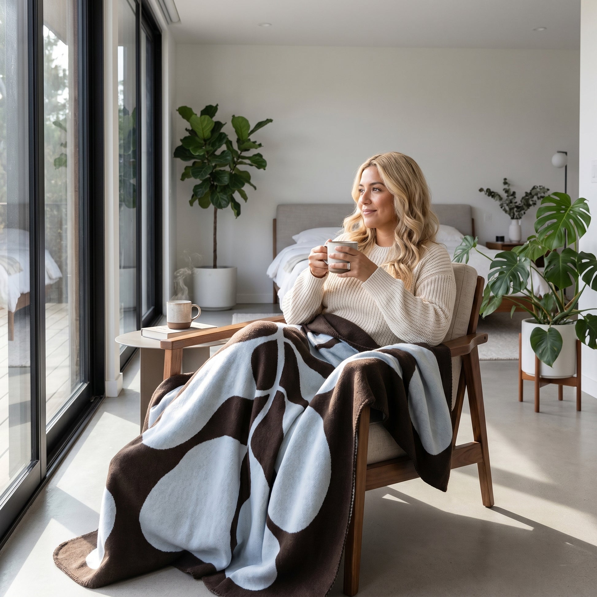 Woman relaxing in a chair, covered by a brown and light blue abstract patterned throw blanket.