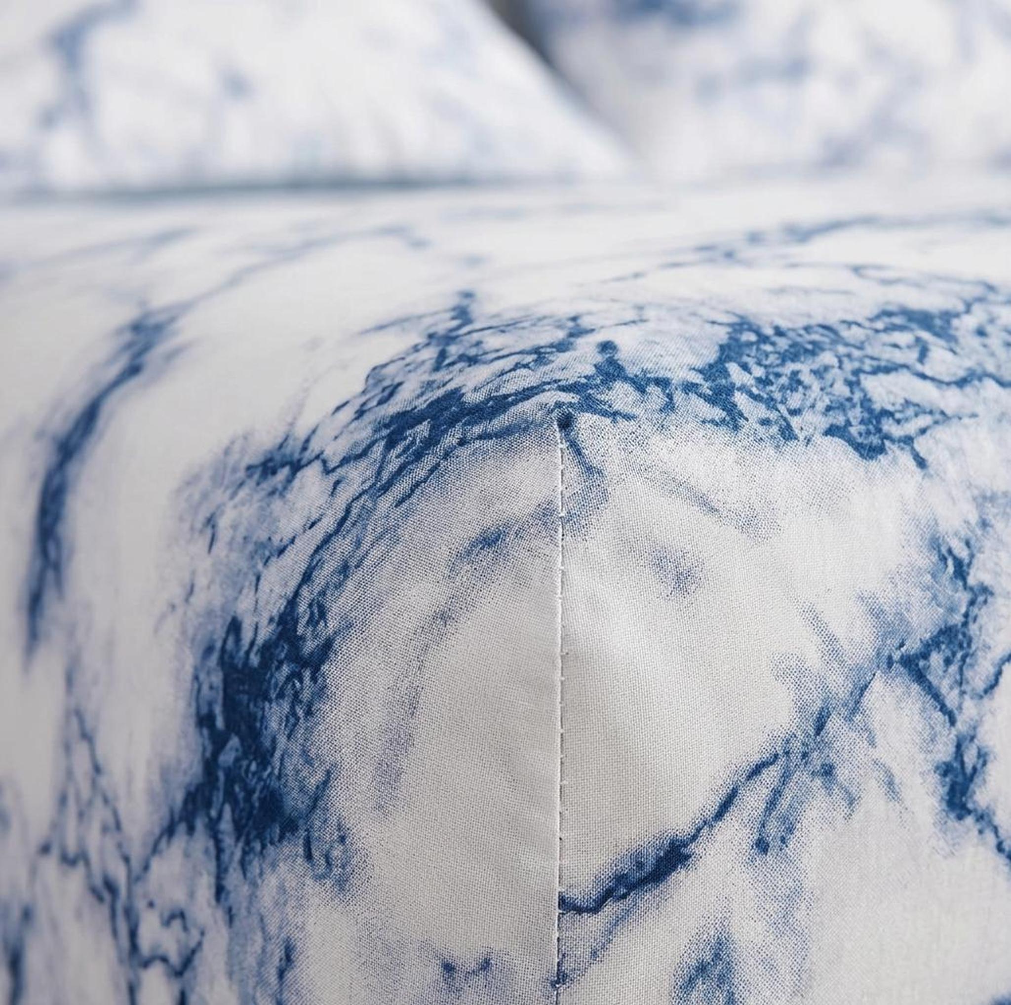 Close-up of a white microfiber fitted sheet with a blue marble print and visible stitching.