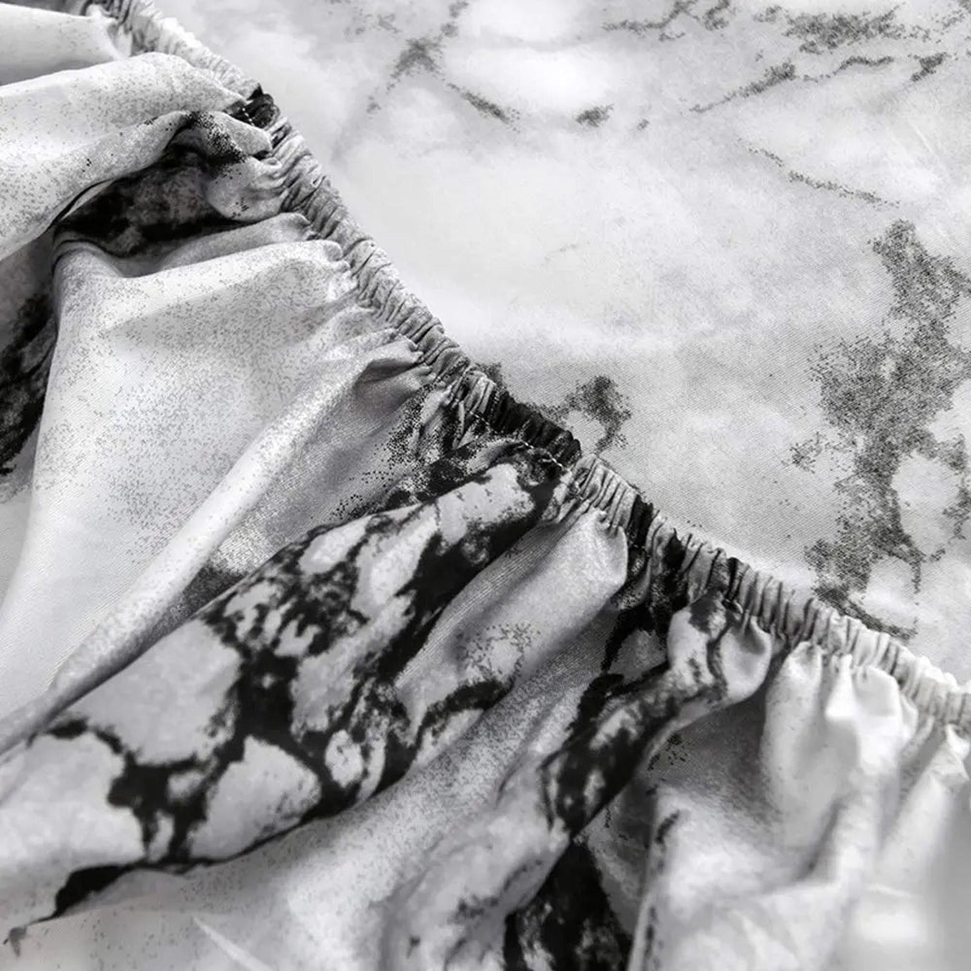Close-up of a white and black marble print microfiber fitted sheet with reinforced elastic edges.