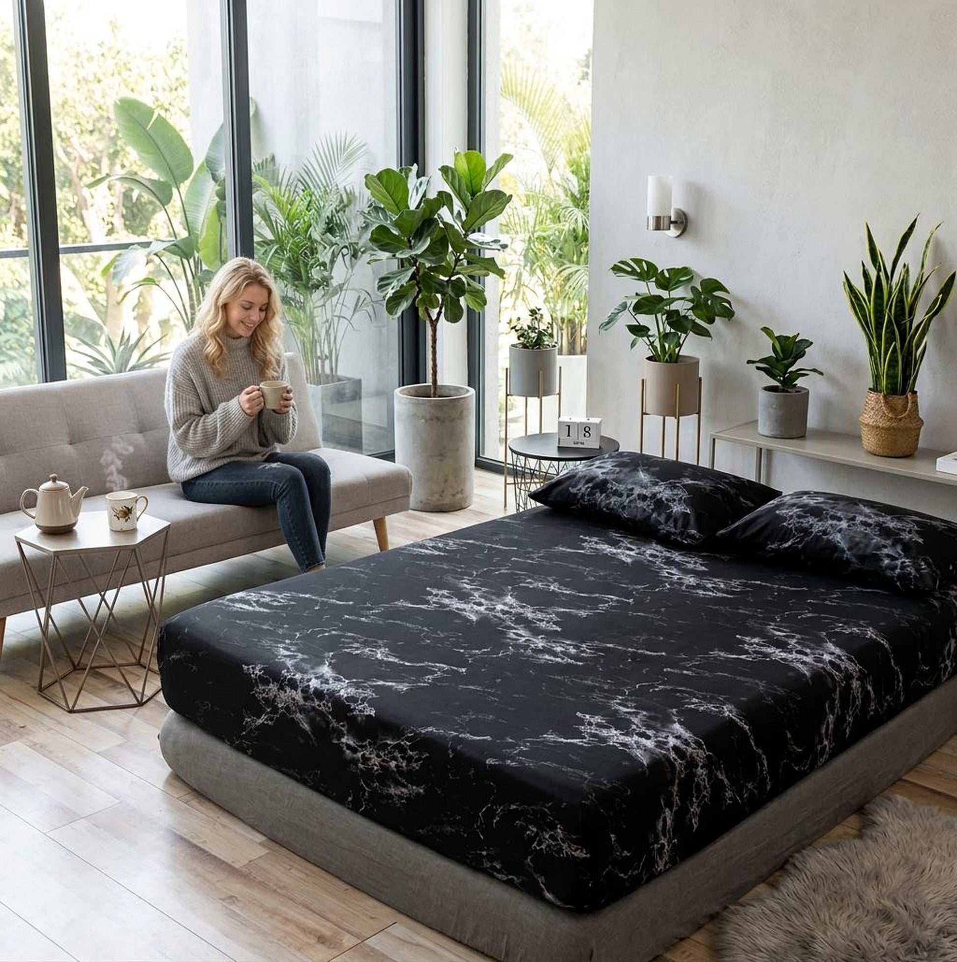 Black microfiber fitted sheet with white marble print on a bed, woman on sofa.