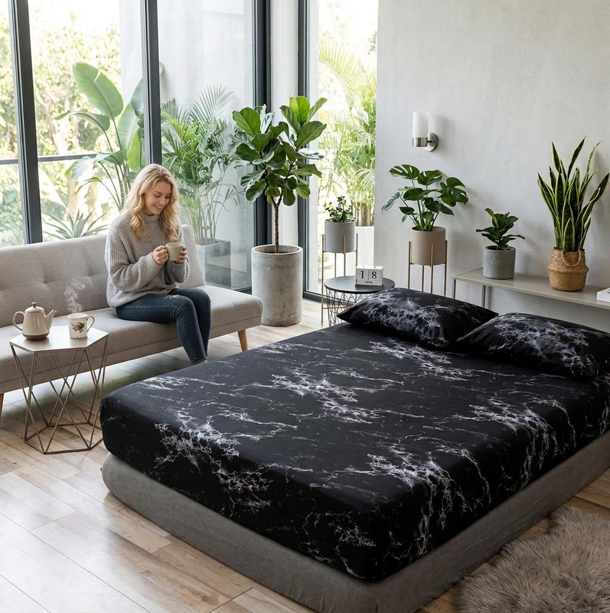 Black microfiber fitted sheet with white marble print on a bed, woman on sofa.