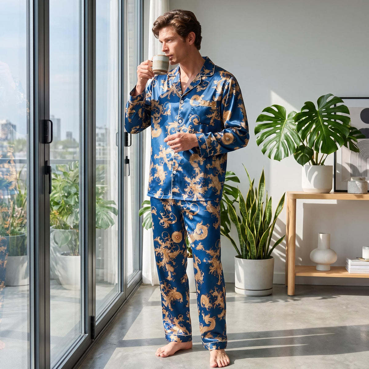Man wearing a blue mulberry silk pajama set with a gold dragon print, notch collar, and button-down top by a bright window.