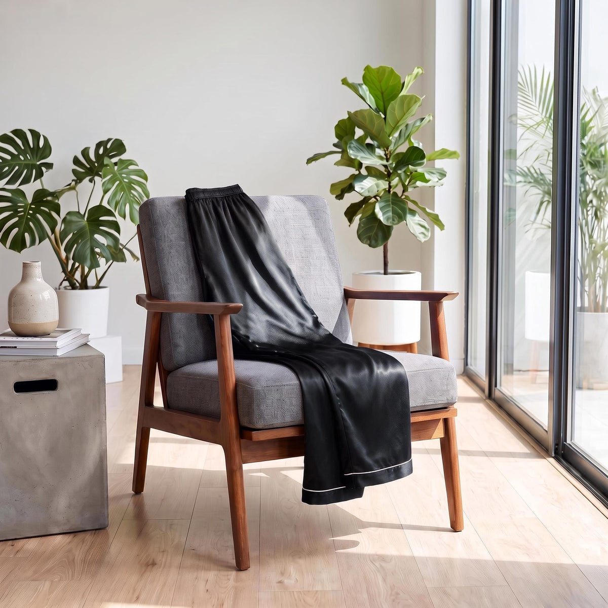 Black mulberry silk pajama pants with an elastic waistband draped over a grey mid-century modern armchair.