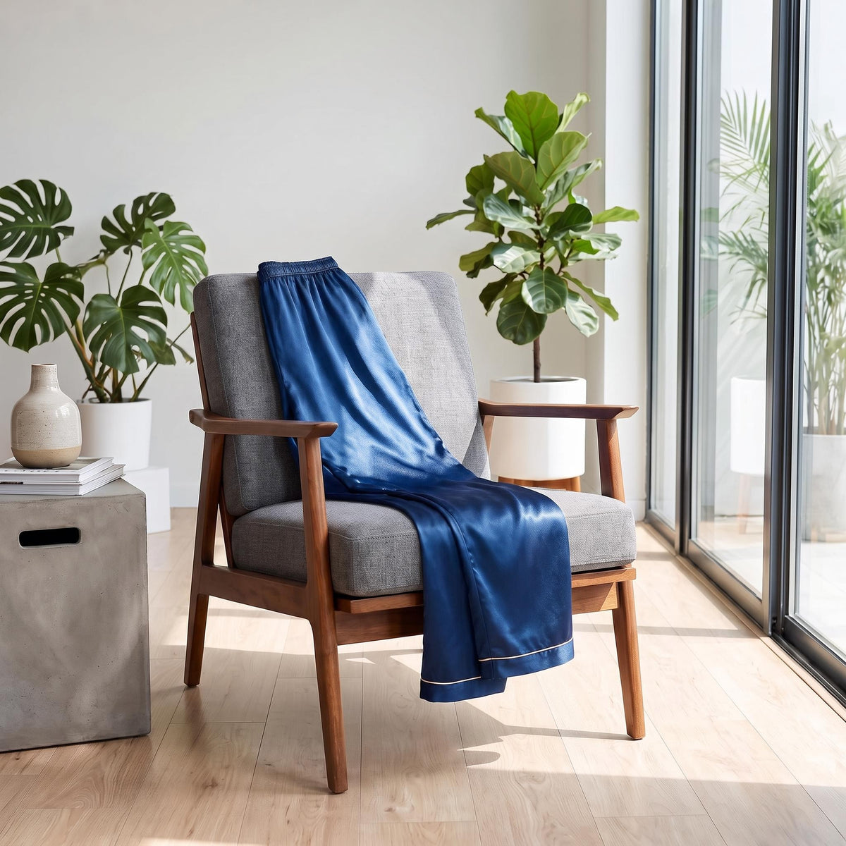 Deep blue mulberry silk pajama pants with an elastic waistband draped over a grey mid-century modern armchair.