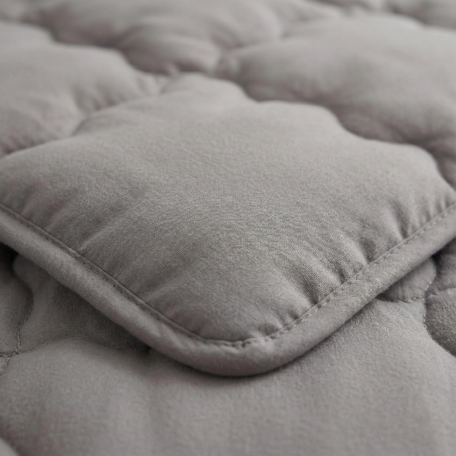 Close-up of a minimalist light gray quilted comforter with soft, breathable fabric and durable stitching.