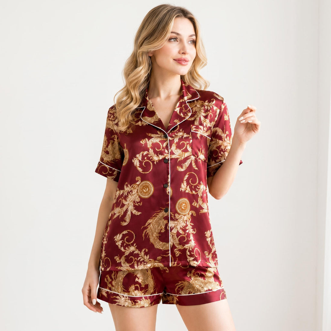 Woman wearing a burgundy mulberry silk pajama short set with a gold dragon print, button-down shirt, and white piping trim.
