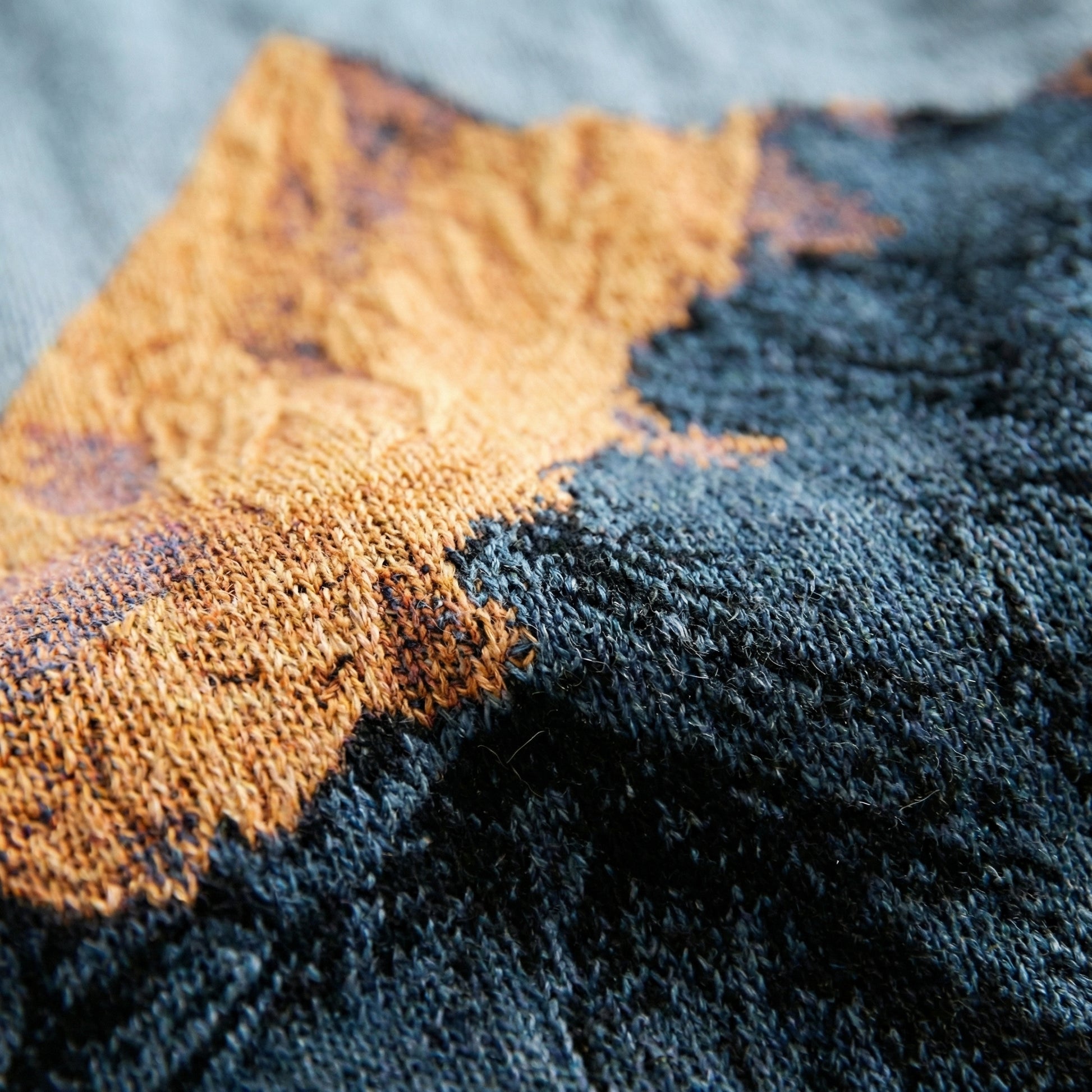 Close-up of a woven natural landscape knitted blanket in orange and dark blue, showcasing its soft texture.