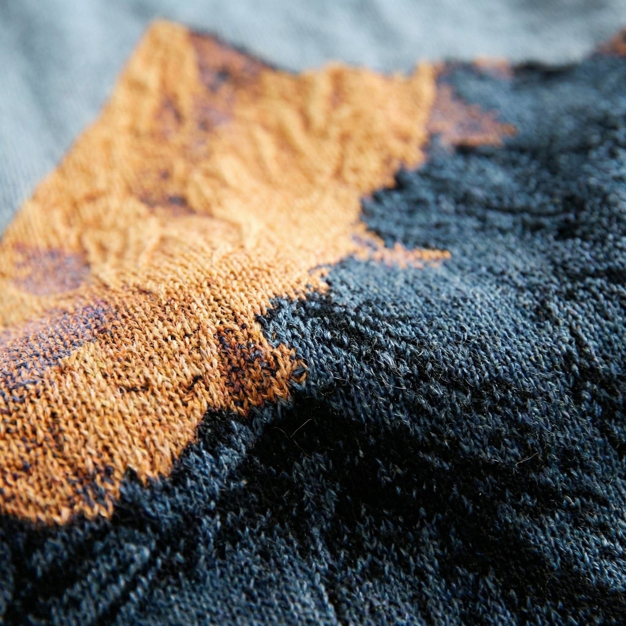 Close-up of a woven natural landscape knitted blanket in orange and dark blue, showcasing its soft texture.