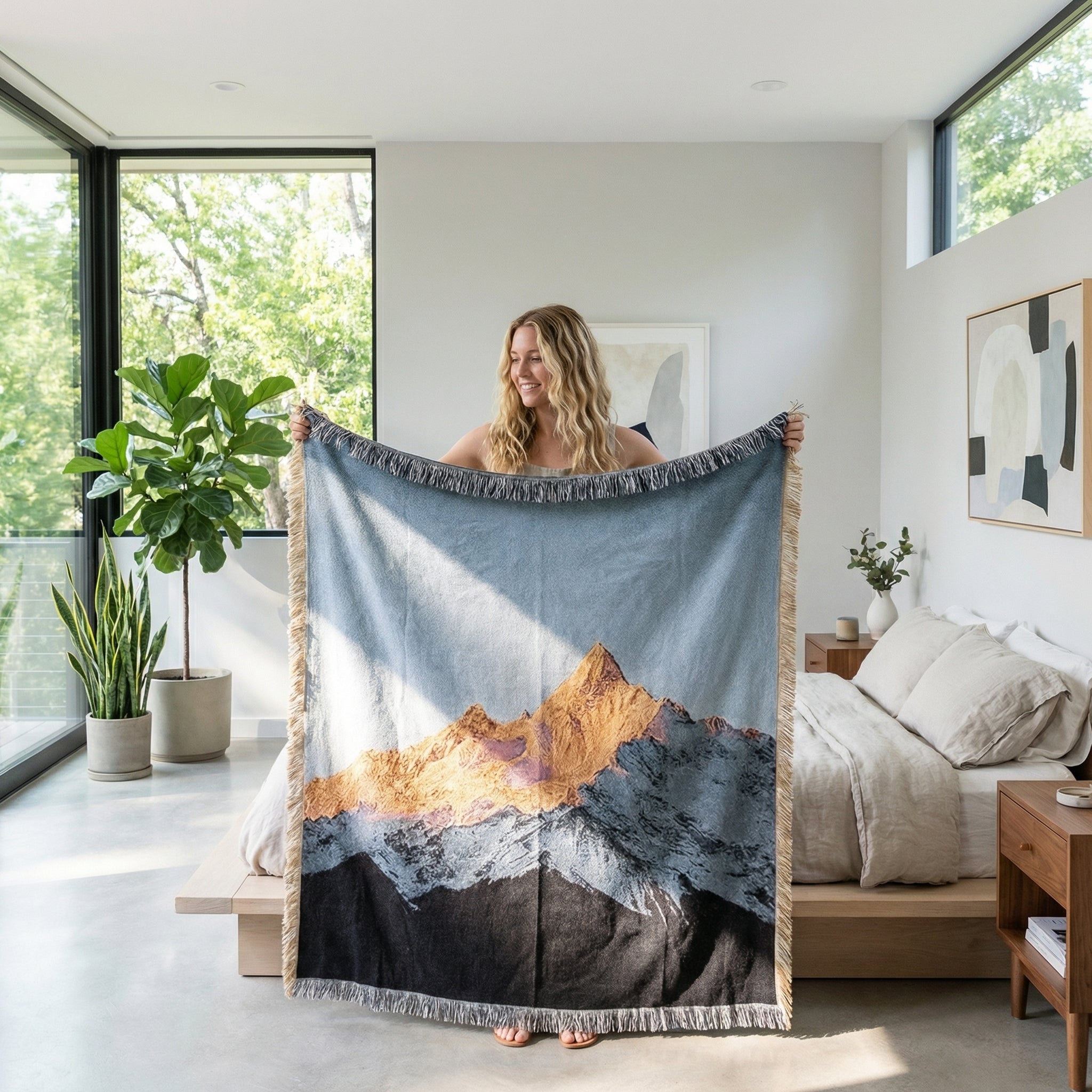 Woman holding a large woven natural landscape blanket with golden mountains and blue sky, featuring fringed edges.