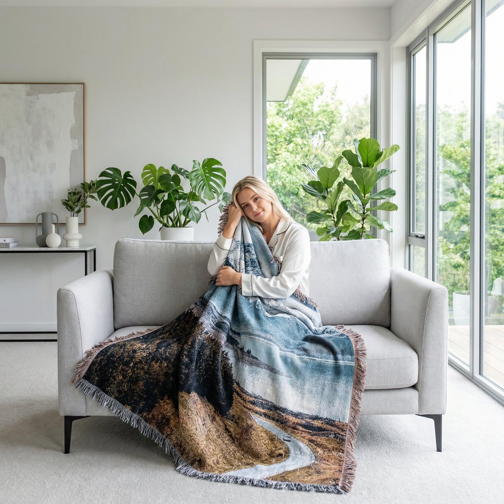 Woman on a sofa covered with a large knitted blanket featuring a natural landscape design.