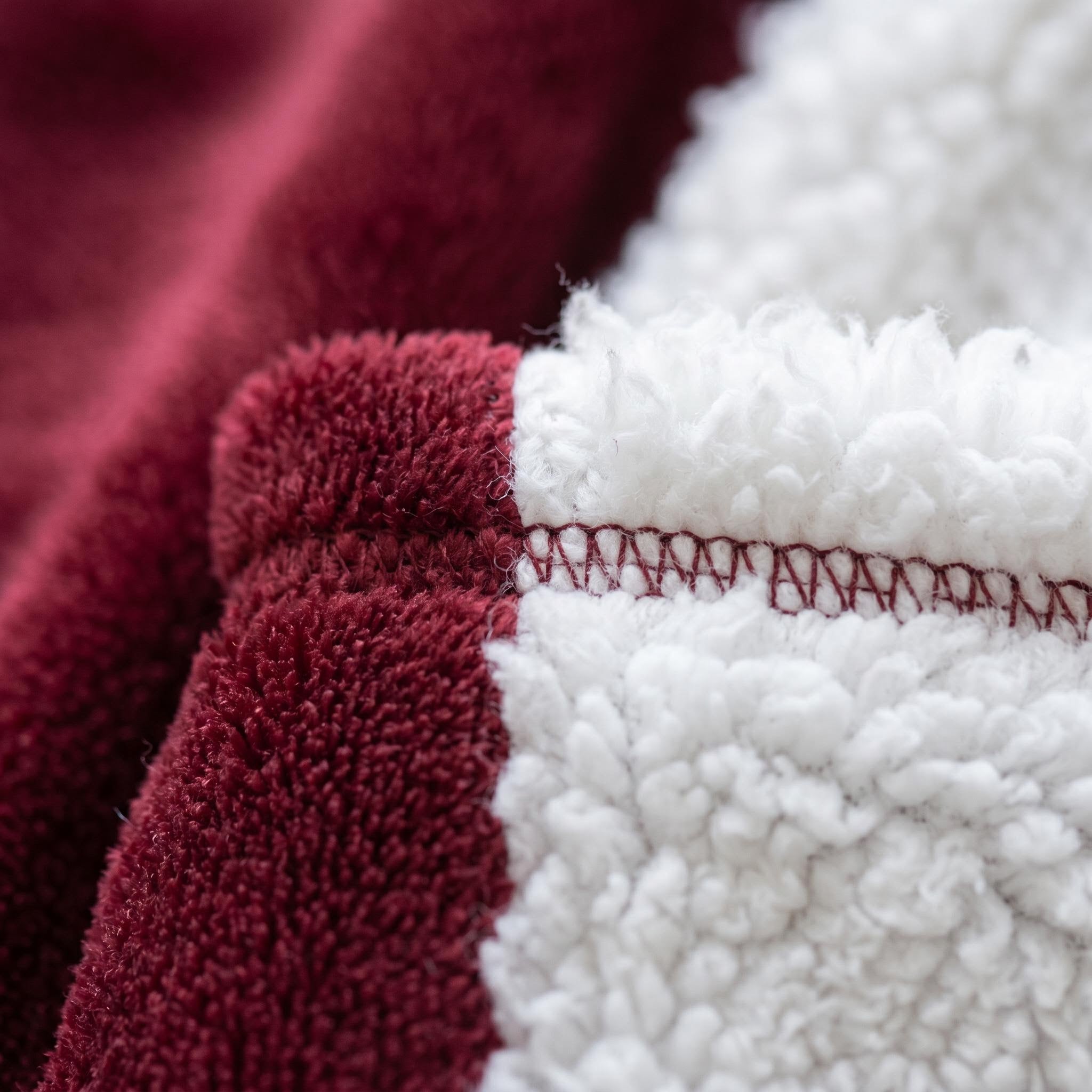 Close-up of a soft, oversized burgundy polyester flannel hooded blanket with white sherpa lining and visible stitching.