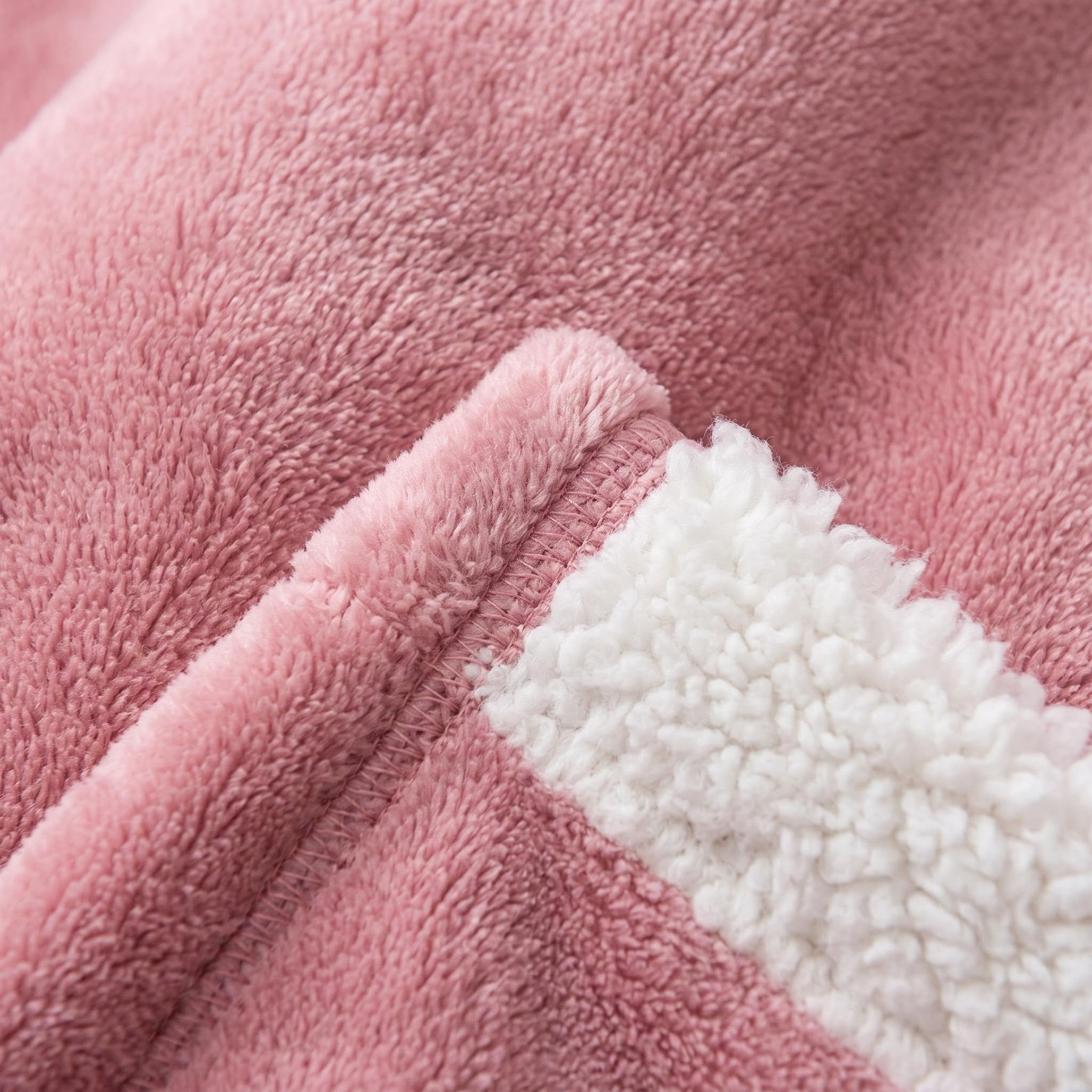 Close-up of a soft, pink polyester flannel oversized hooded blanket with a white sherpa lining.