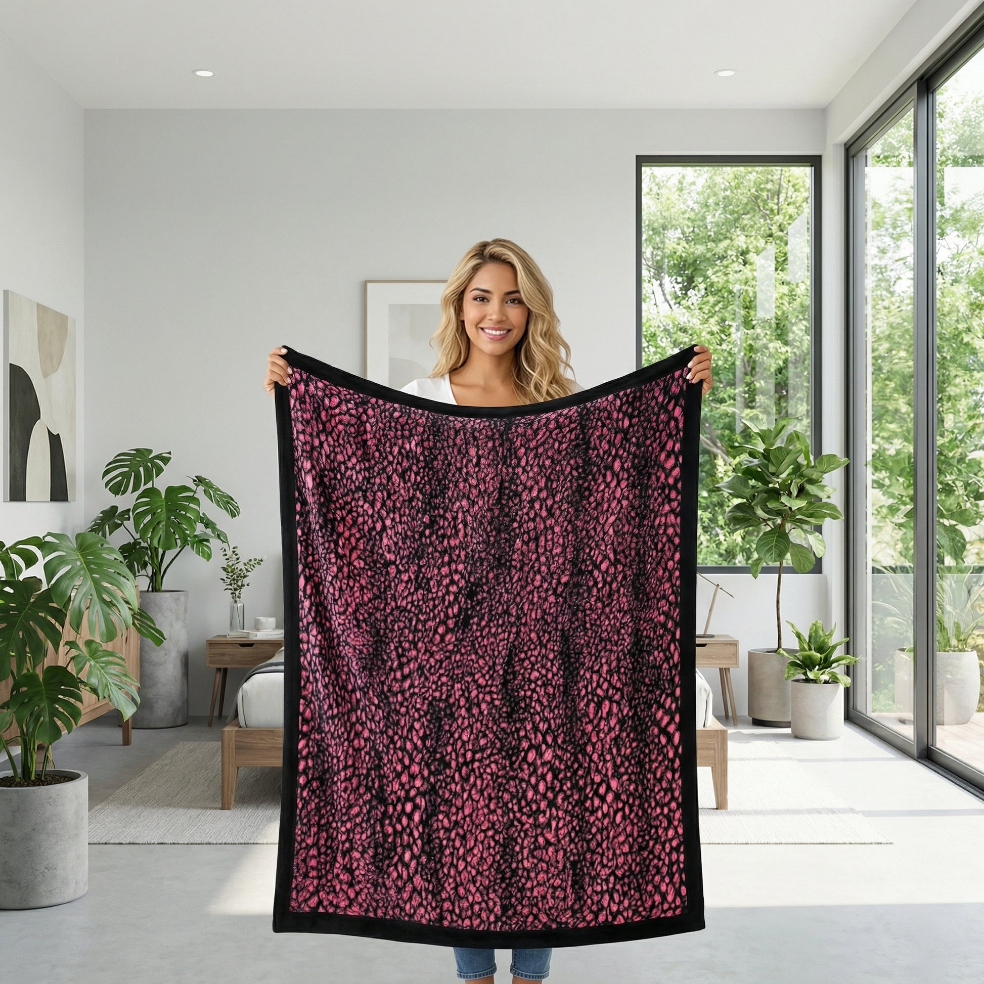Smiling woman holding up a soft, plush pink leopard print blanket with a black border in a modern room.