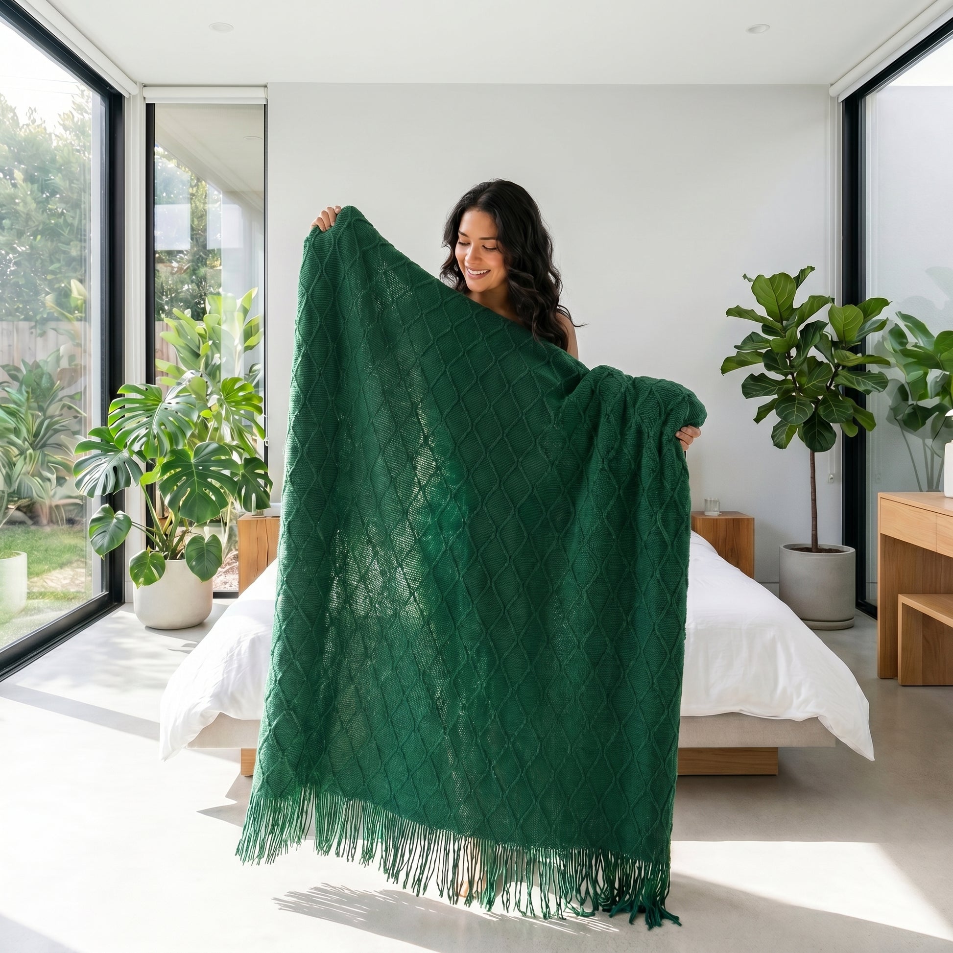 Woman holding a soft, dark green knitted throw blanket with a textured diamond pattern and tassels.