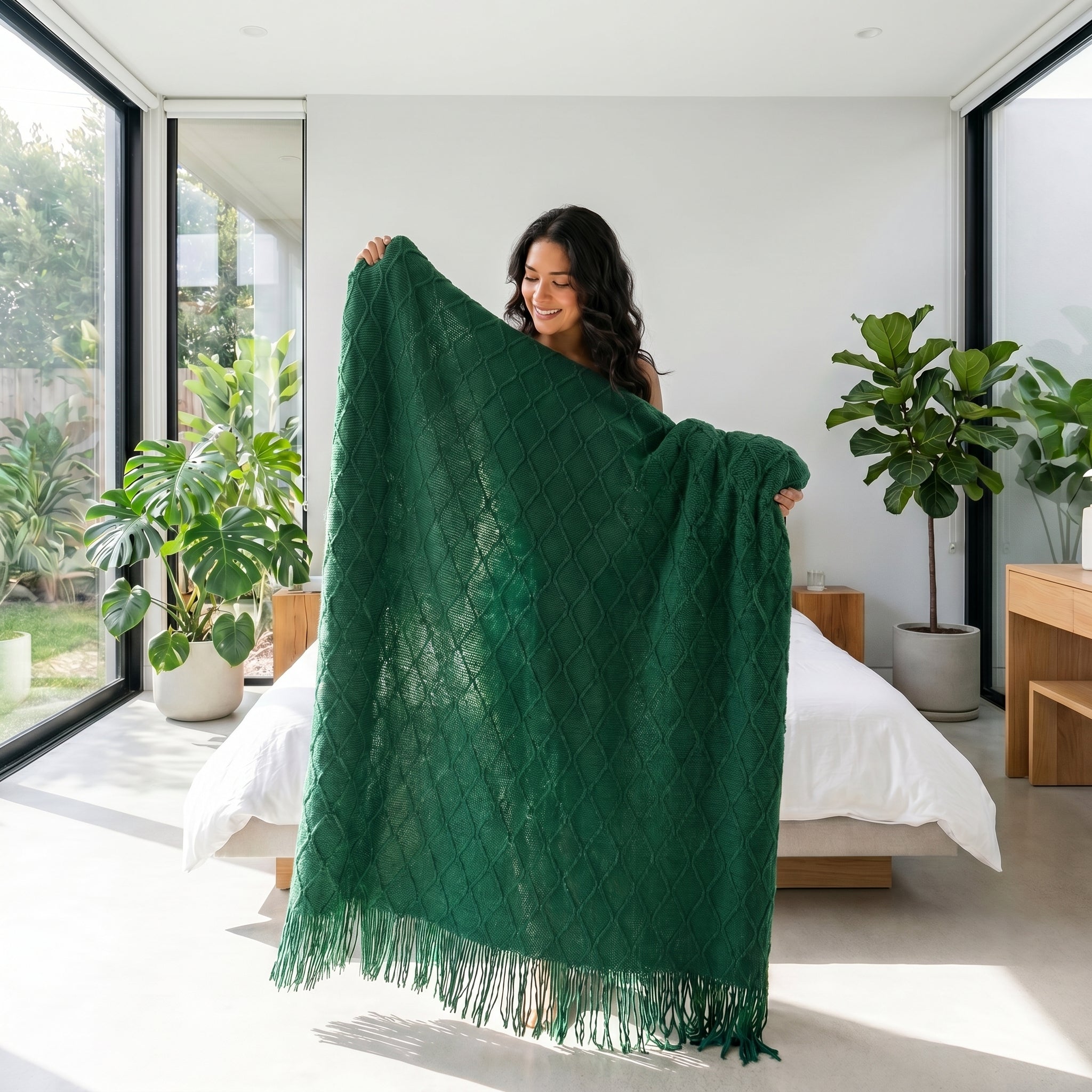 Woman holding a soft, dark green knitted throw blanket with a textured diamond pattern and tassels.