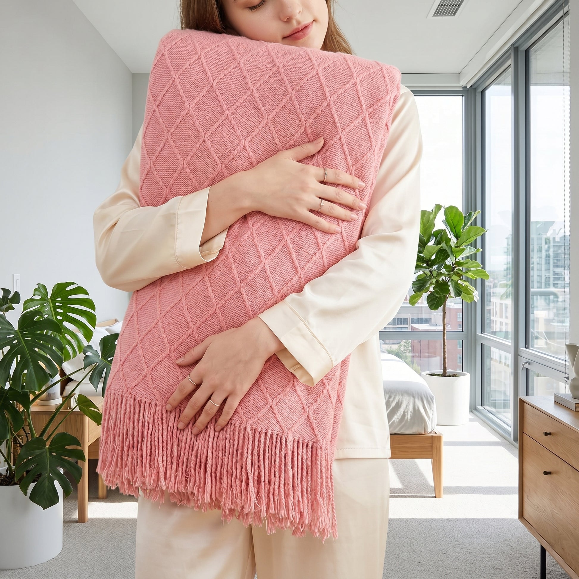 Woman in pajamas hugging a soft pink knit throw blanket with diamond plaid pattern and tassels.