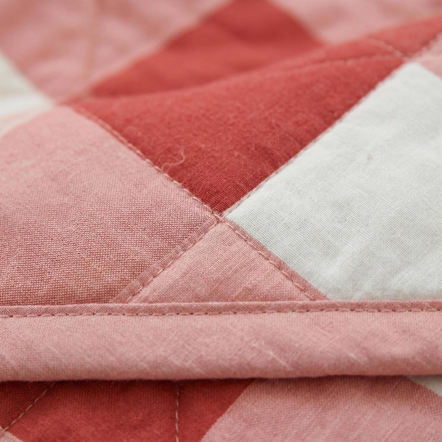 Close-up of a pink, red, and white plaid lightweight summer quilt made of soft, breathable polyester.