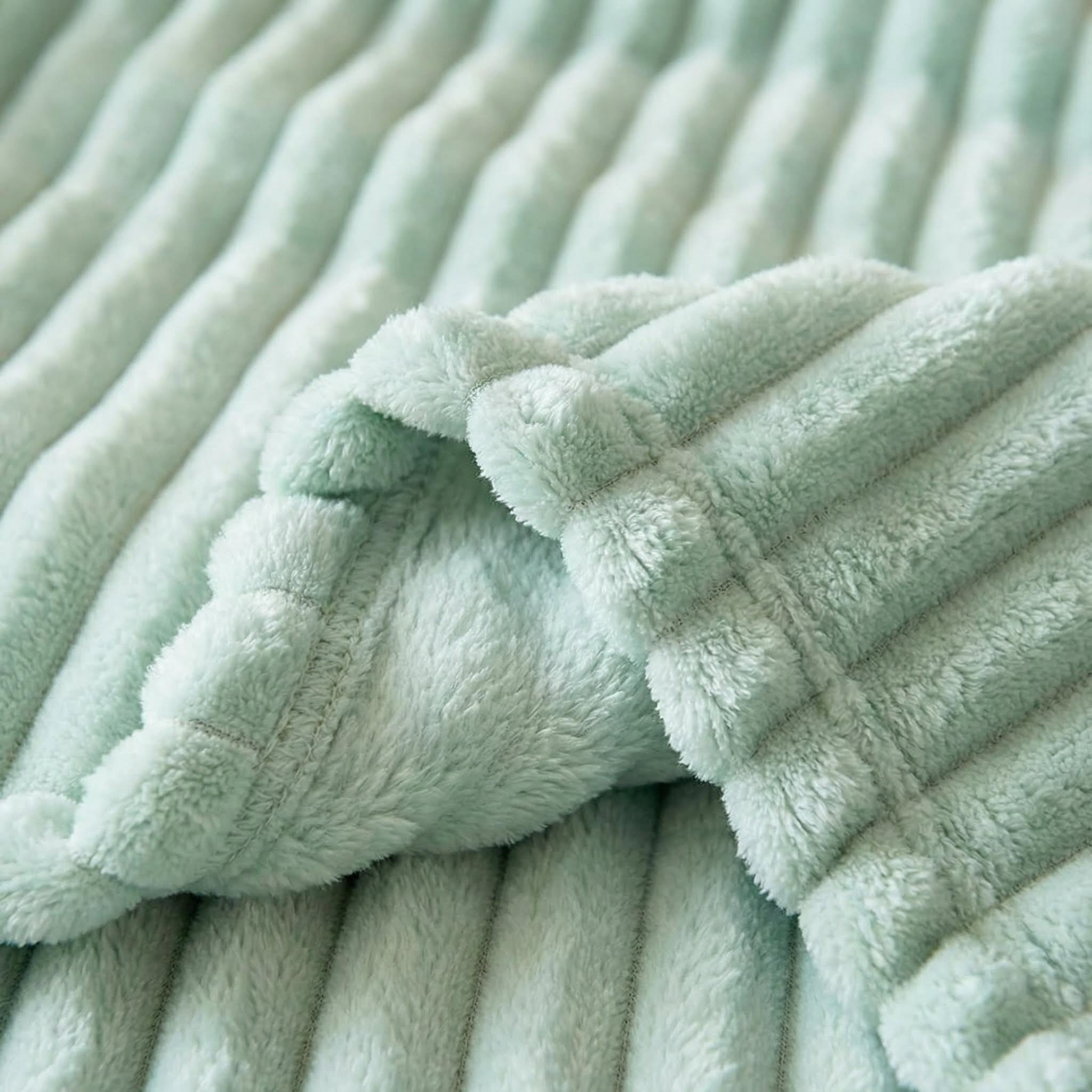 Plush faux fur throw blanket in light green with a soft, ribbed striped texture.