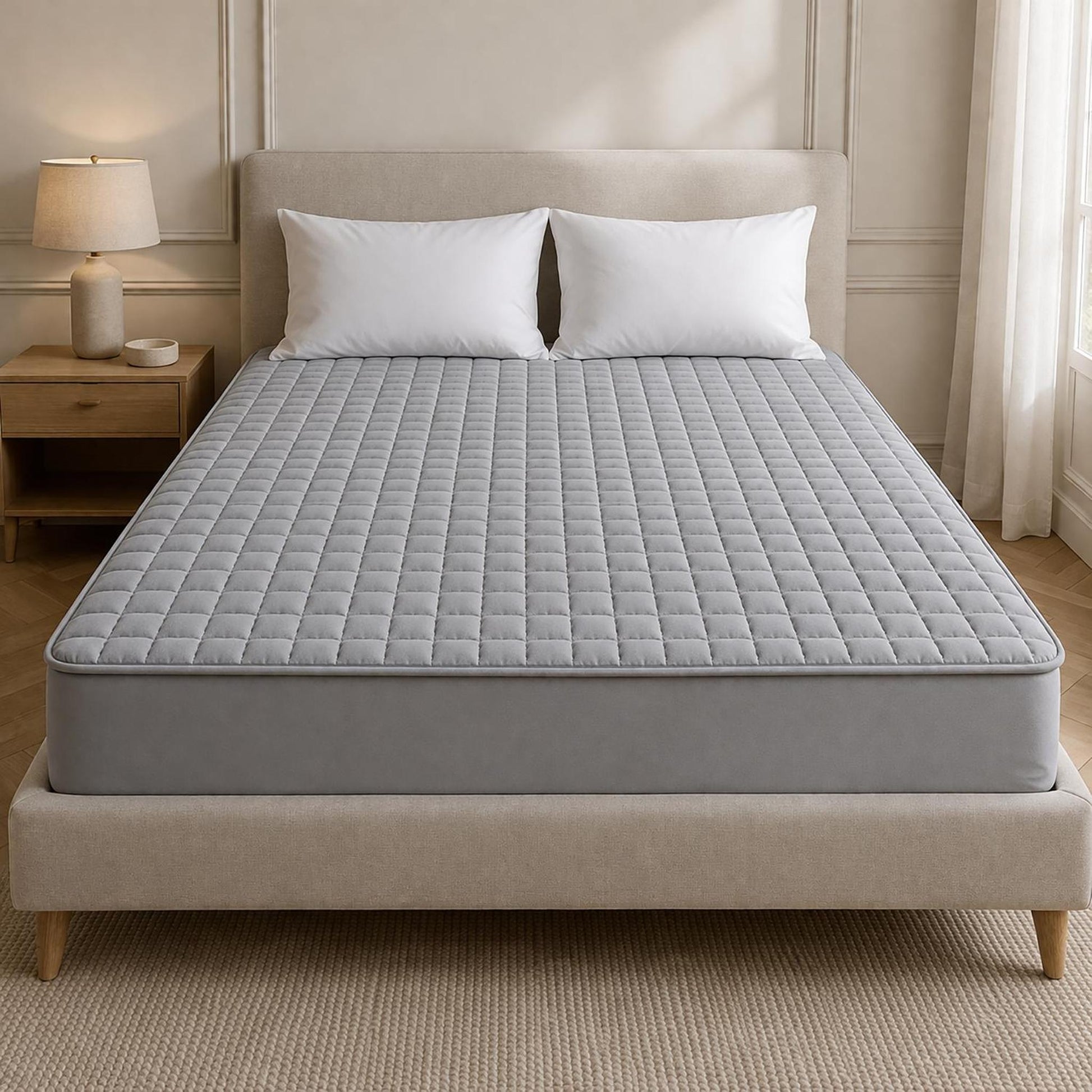 Gray quilted queen mattress protector on a bed with white pillows, showcasing its soft, square-stitched design.