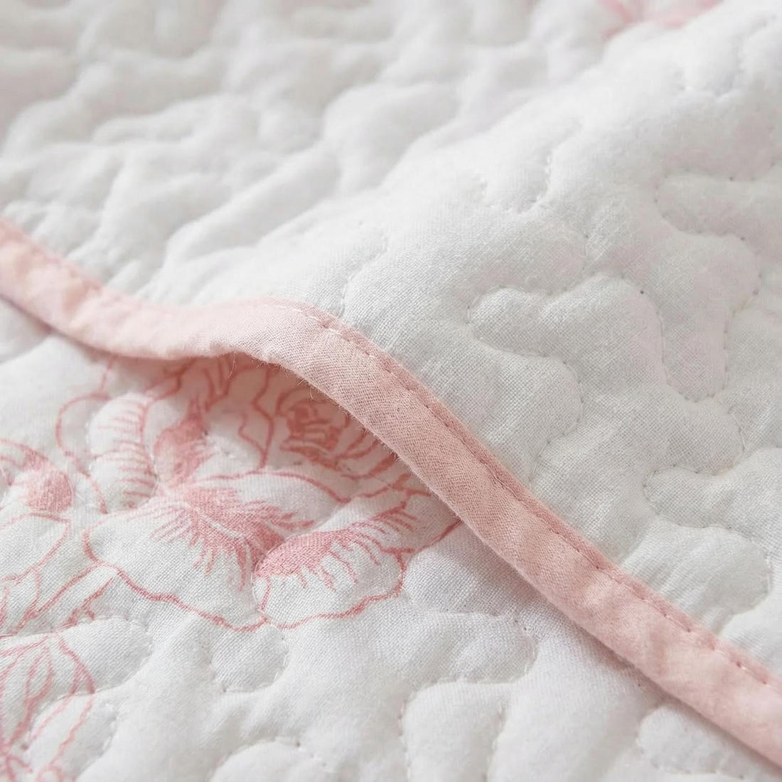 Woman placing a Queen size rose print quilted bedding set with white and pink floral design on a bed.
