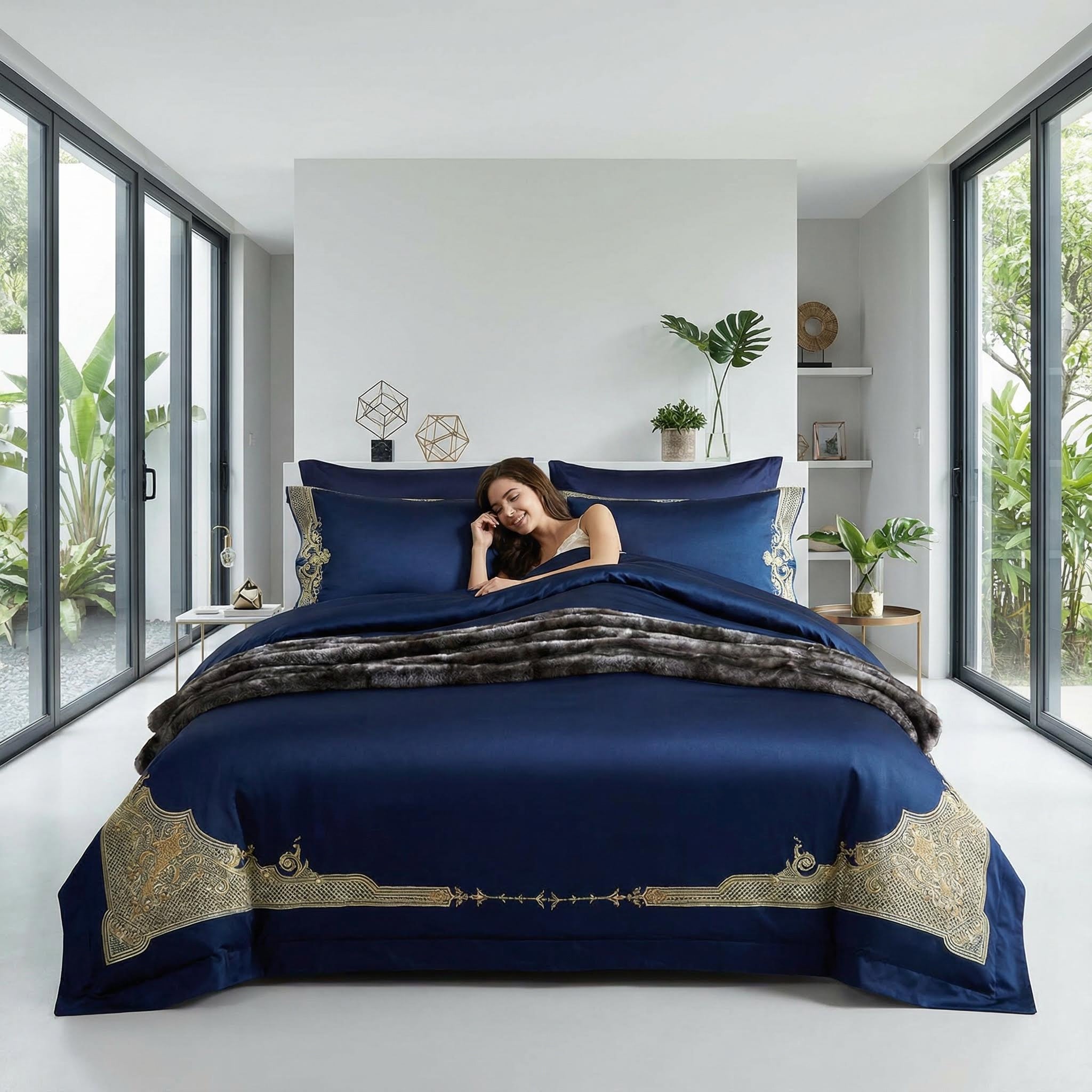 Royal blue cotton bedding set with gold embroidery, a woman relaxing in bed.